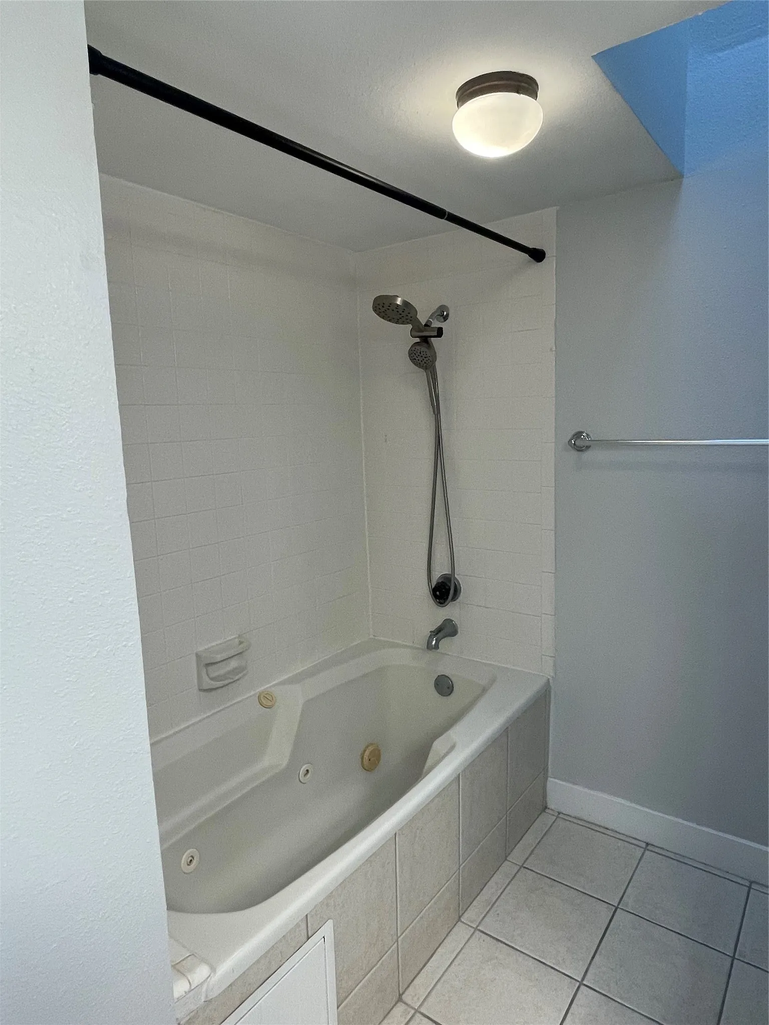 Jetted bathtub with white subway tile surround, tiled flooring, and a ceiling-mounted light fixture