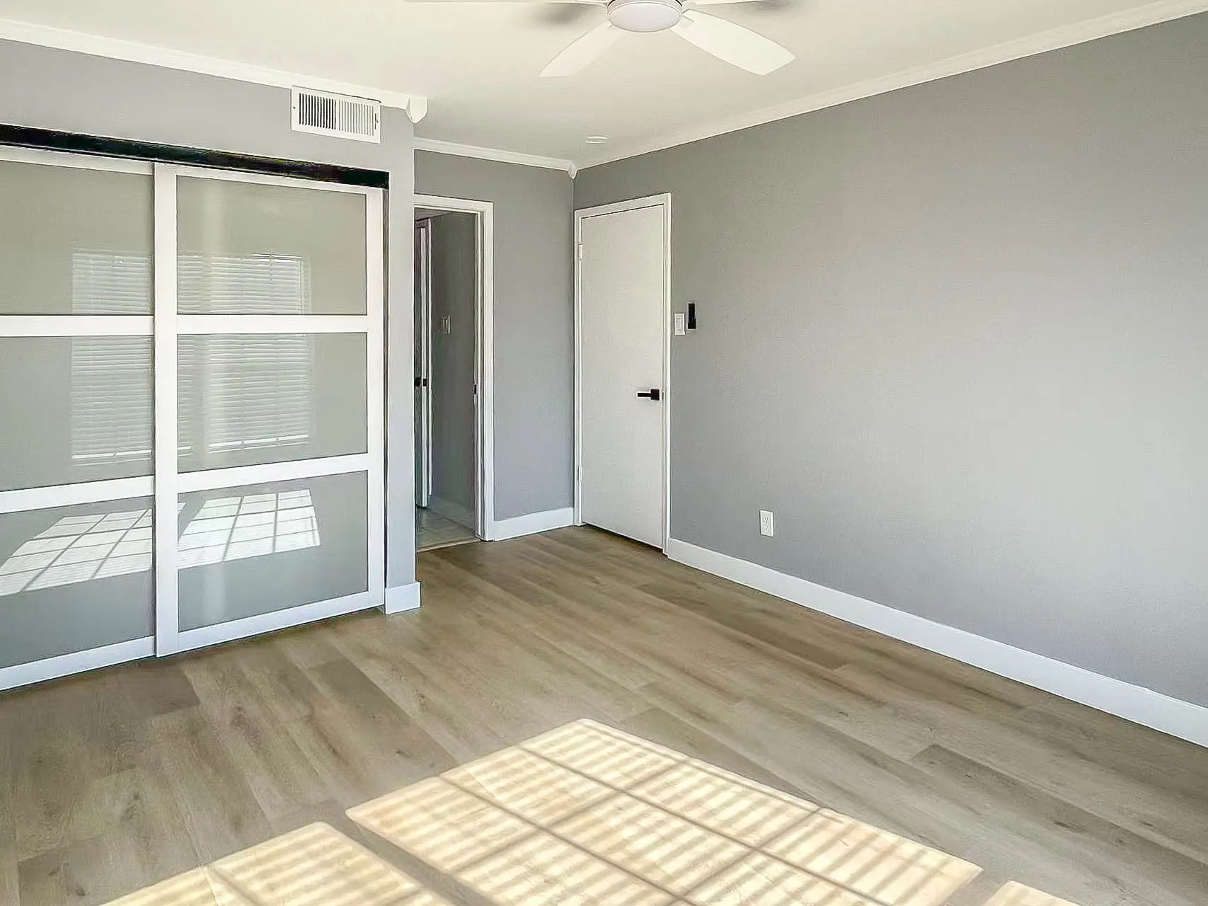 Wood-finish flooring, white crown molding, and a ceiling fan with light fixture
