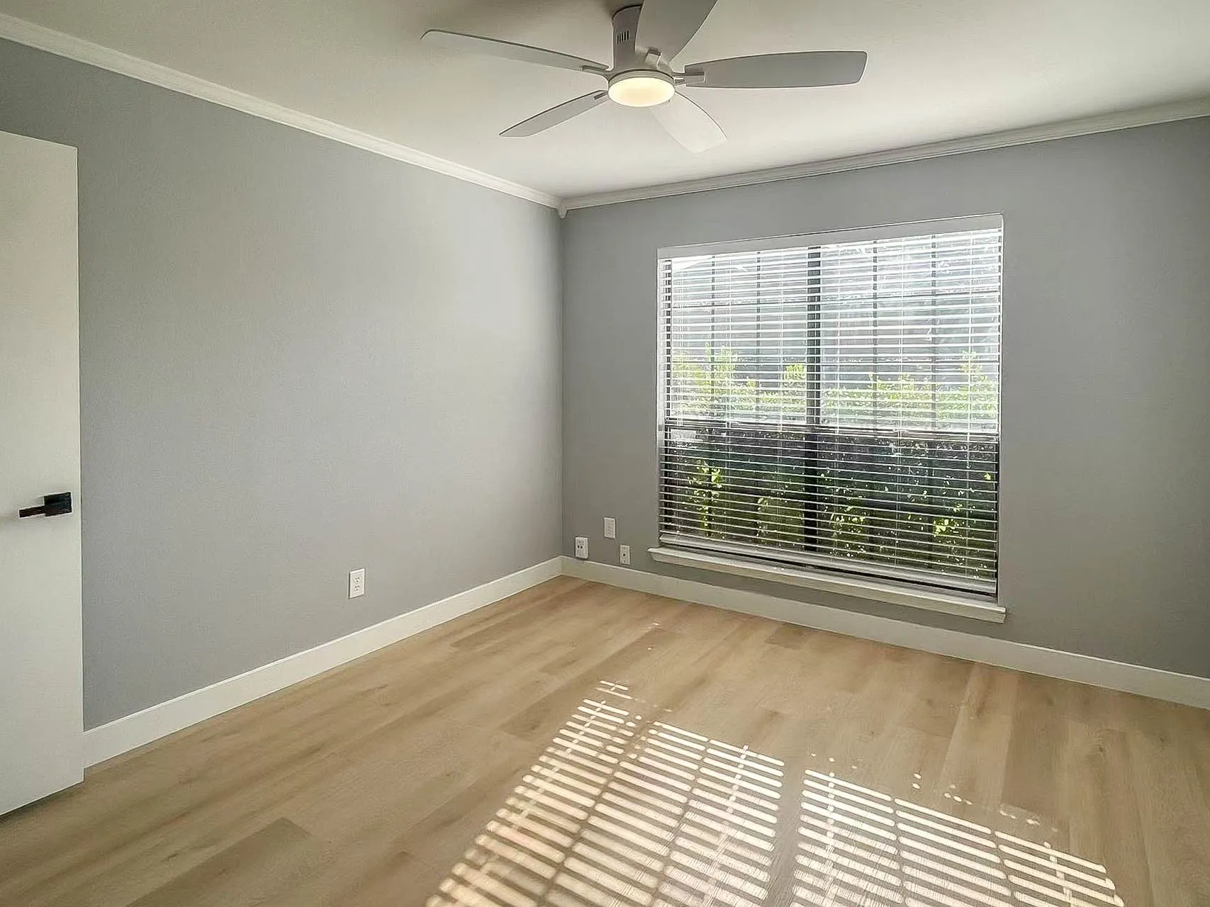 Spacious room featuring wood-finish flooring, a contemporary ceiling fan, and a large window with horizontal blinds