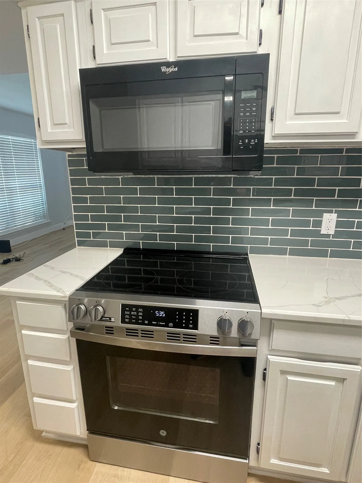 White cabinetry with black hardware, subway tile backsplash, white countertops, stainless steel range with black cooktop, and an over-the-range microwave