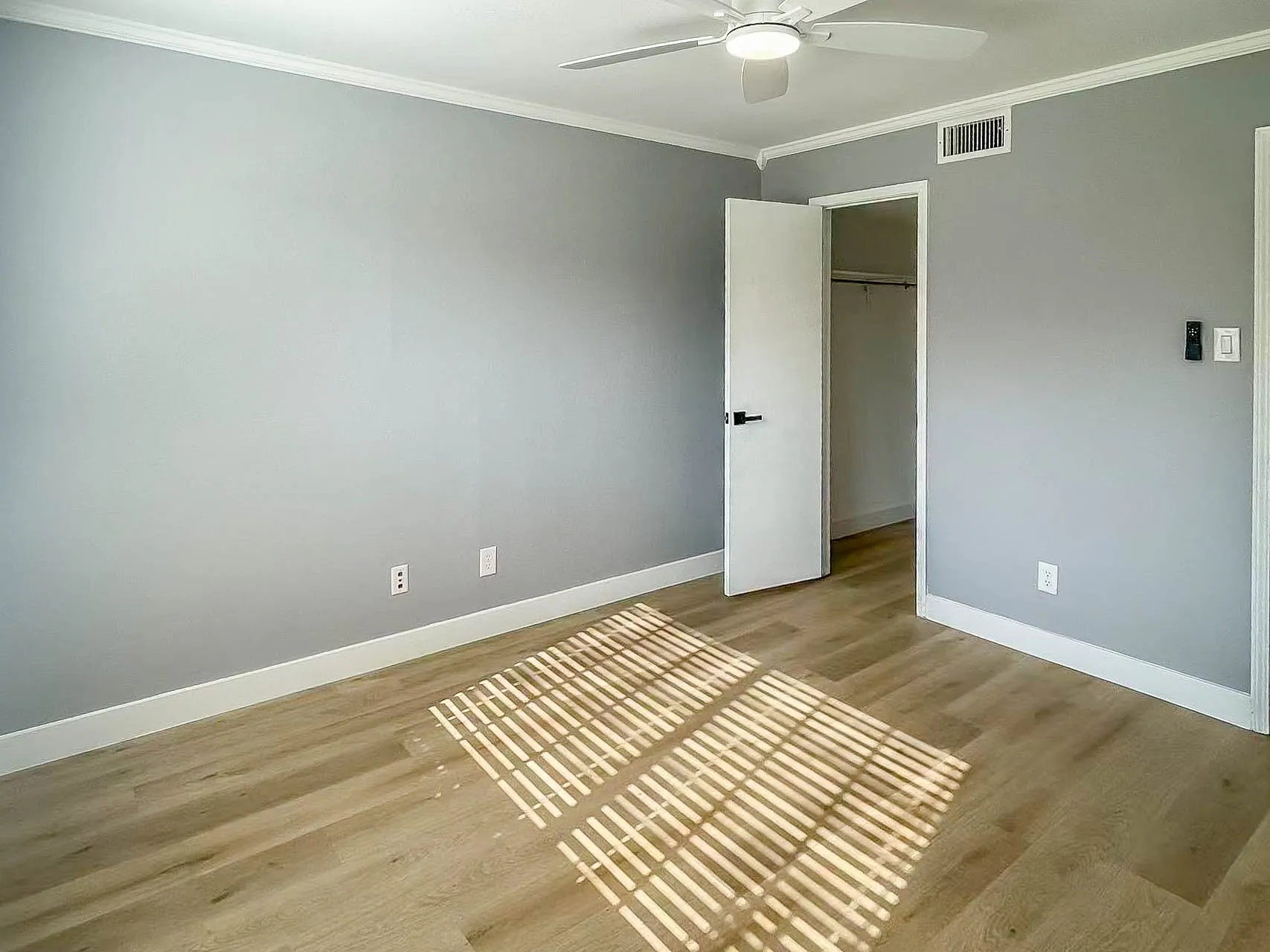 Wood-finish flooring, ceiling fan with integrated lighting, crown molding, and a neutral wall palette