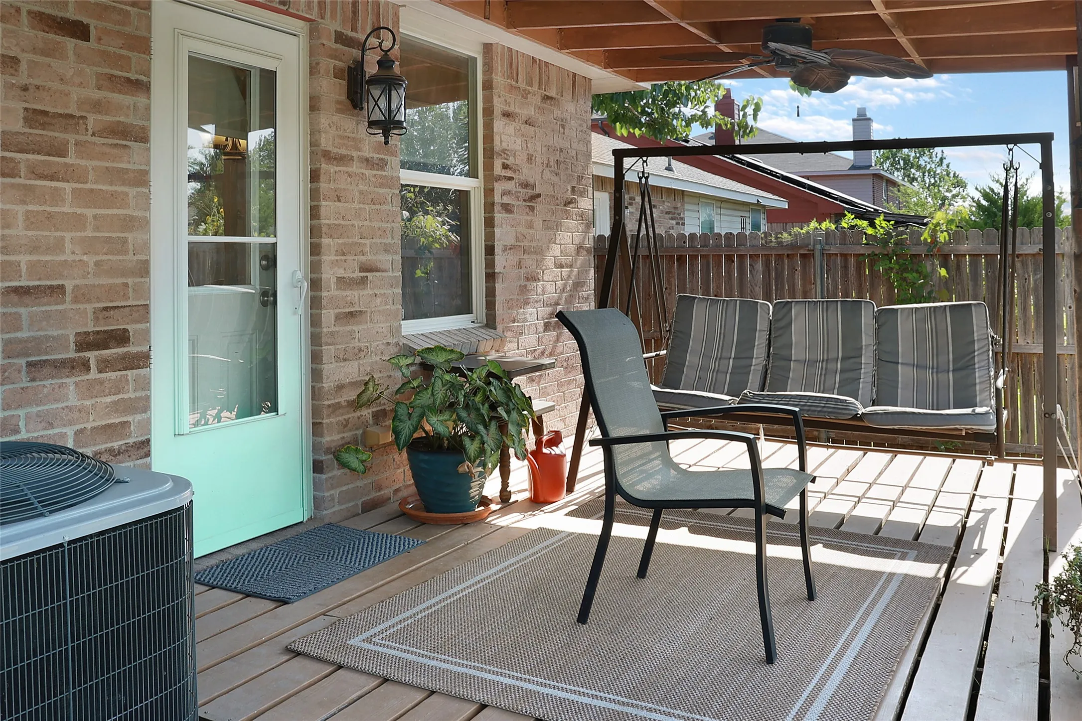 Covered porch featuring a wood-plank deck, brick exterior, and a ceiling fan