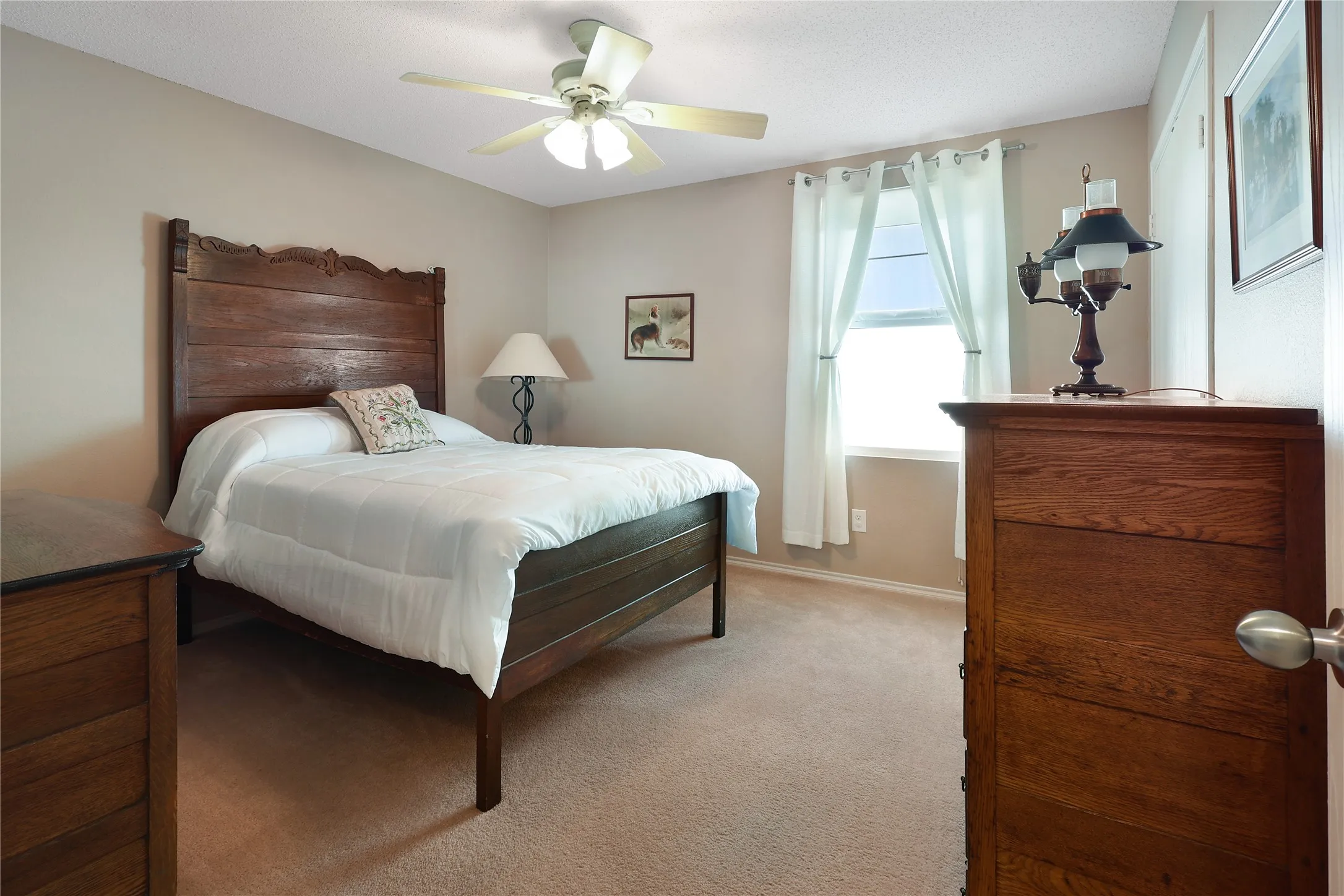 Carpeted room featuring a ceiling fan with integrated lighting and a window with white curtains