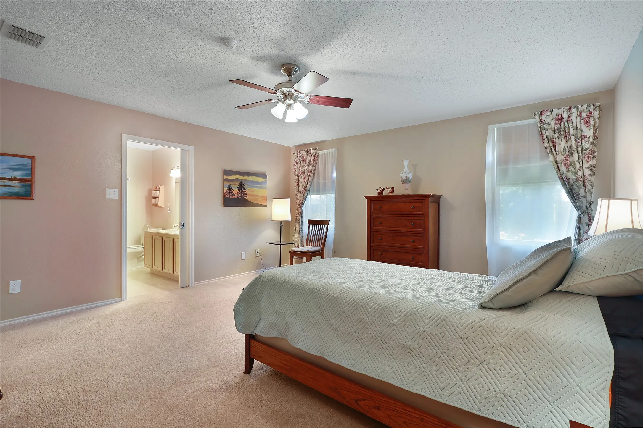 Plush carpeting throughout, ceiling fan with integrated lighting, and direct access to an attached bathroom featuring a vanity