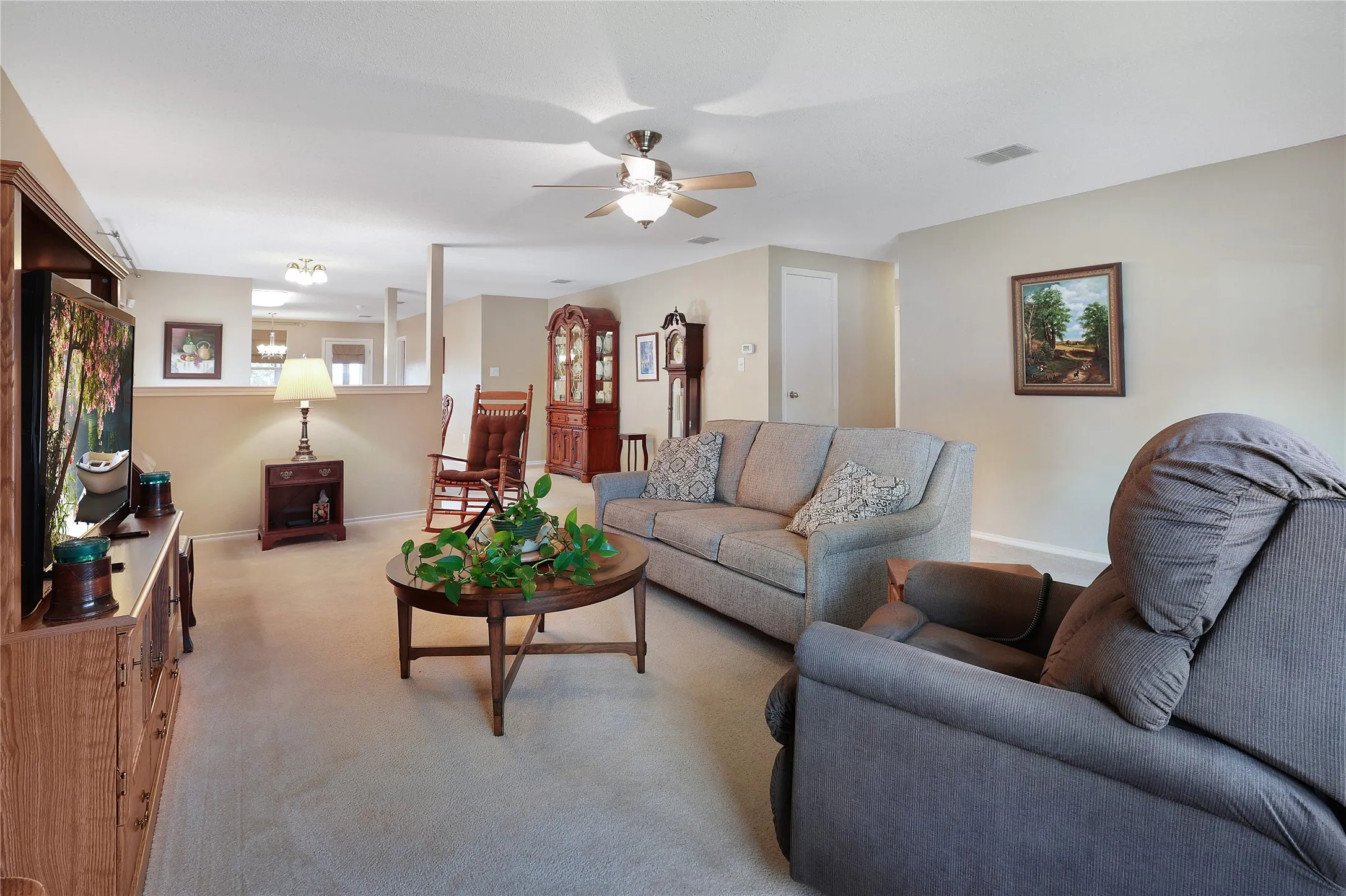 Open-concept living area featuring a ceiling fan, neutral wall tones, and carpeted flooring