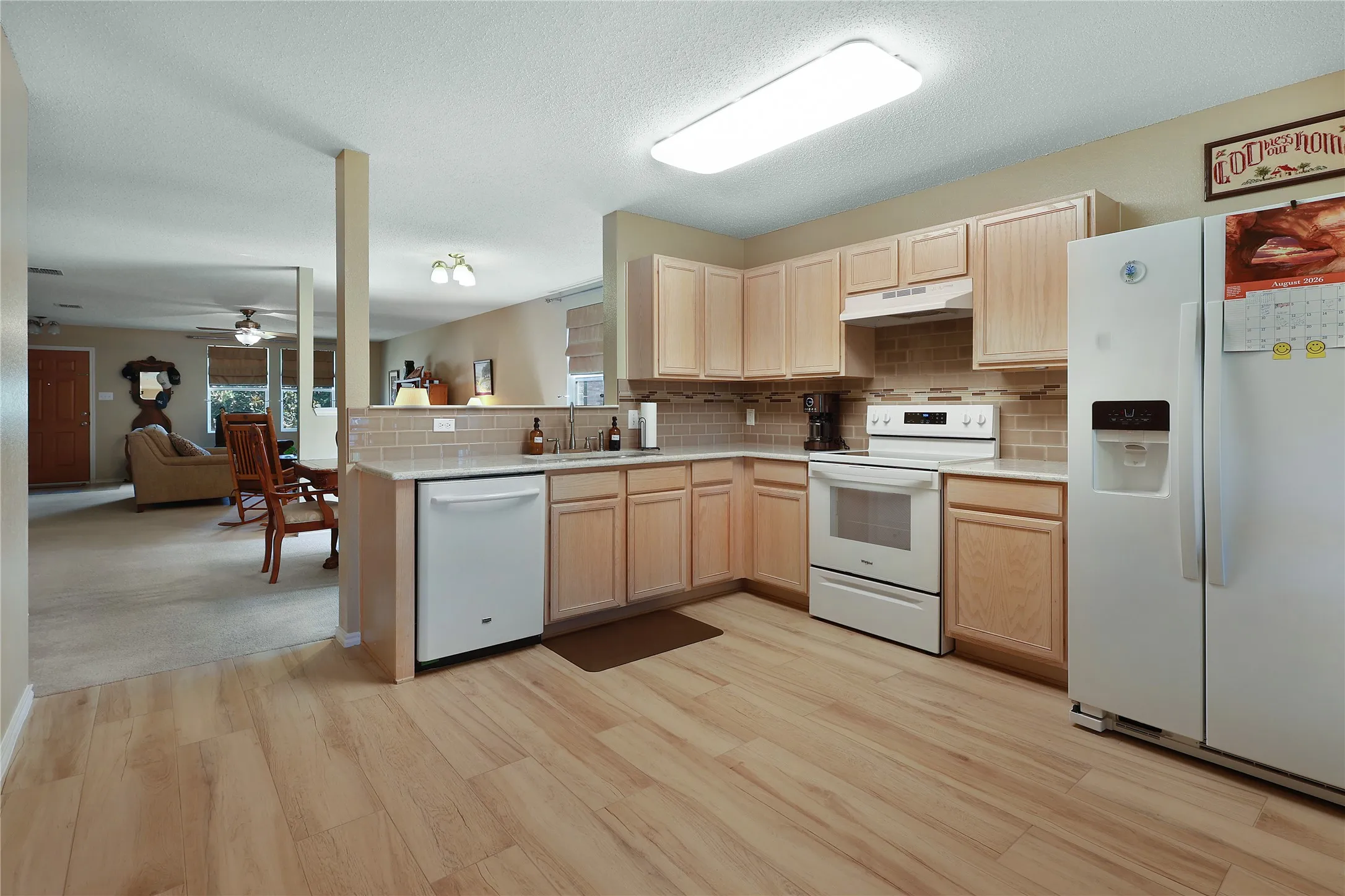 Kitchen featuring wood-finish flooring, light wood cabinetry, white appliances, and a tiled backsplash