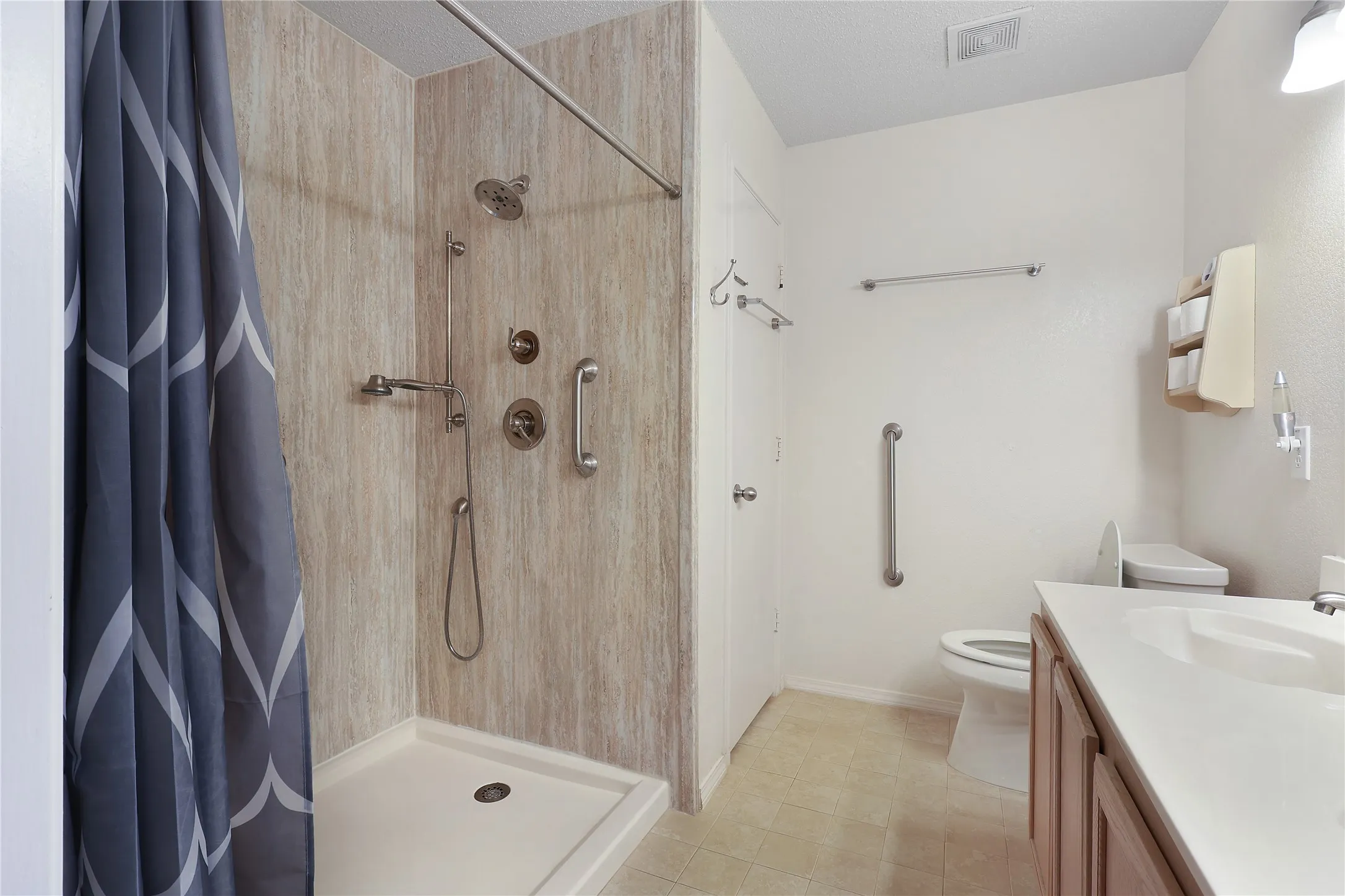 Shower with a wood-finish surround and multiple showerheads, light wood-finish vanity with an integrated sink, and light-toned flooring