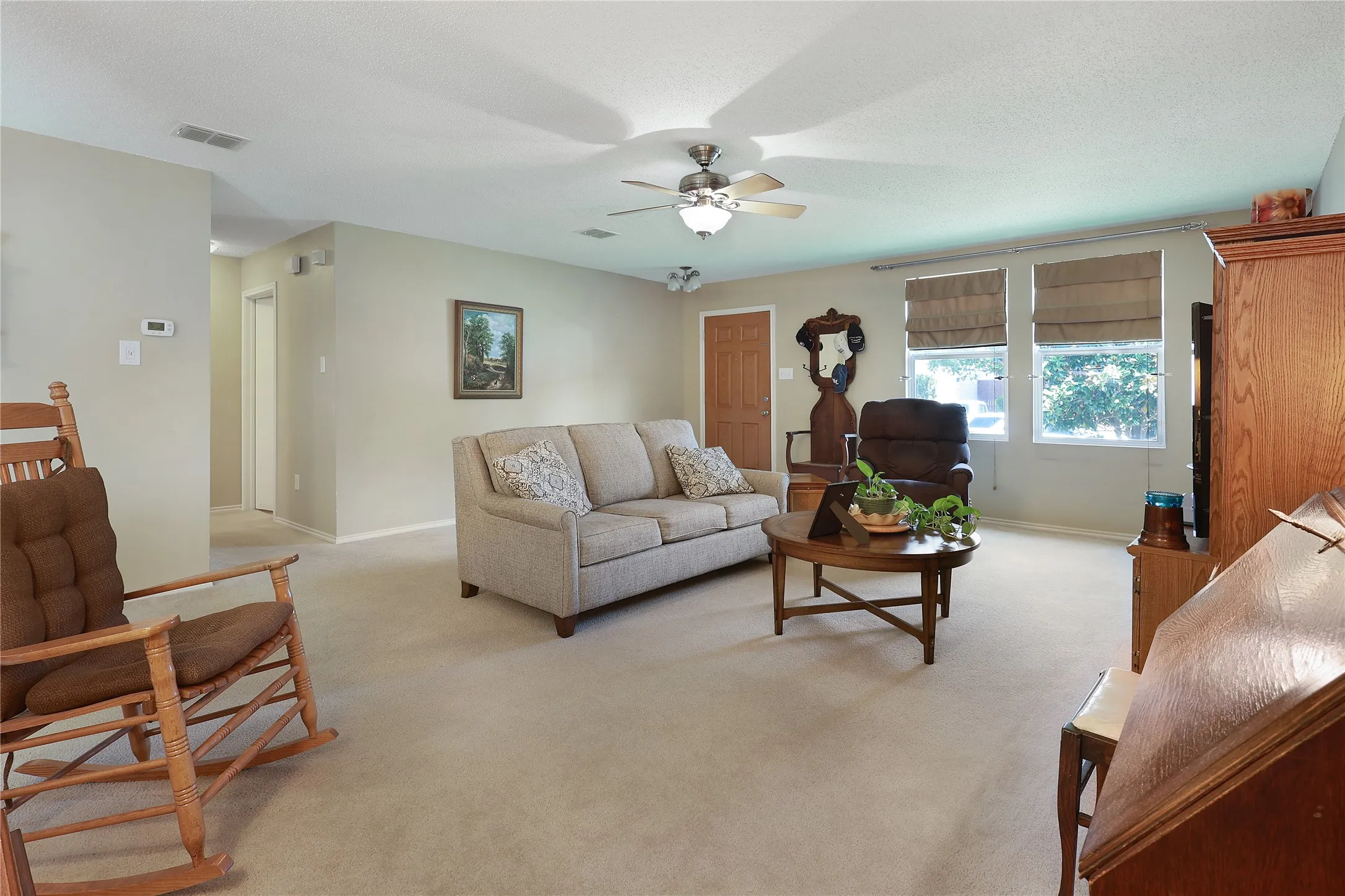 Carpeted living area with light neutral wall tones, multiple windows, and a ceiling fan with integrated lighting