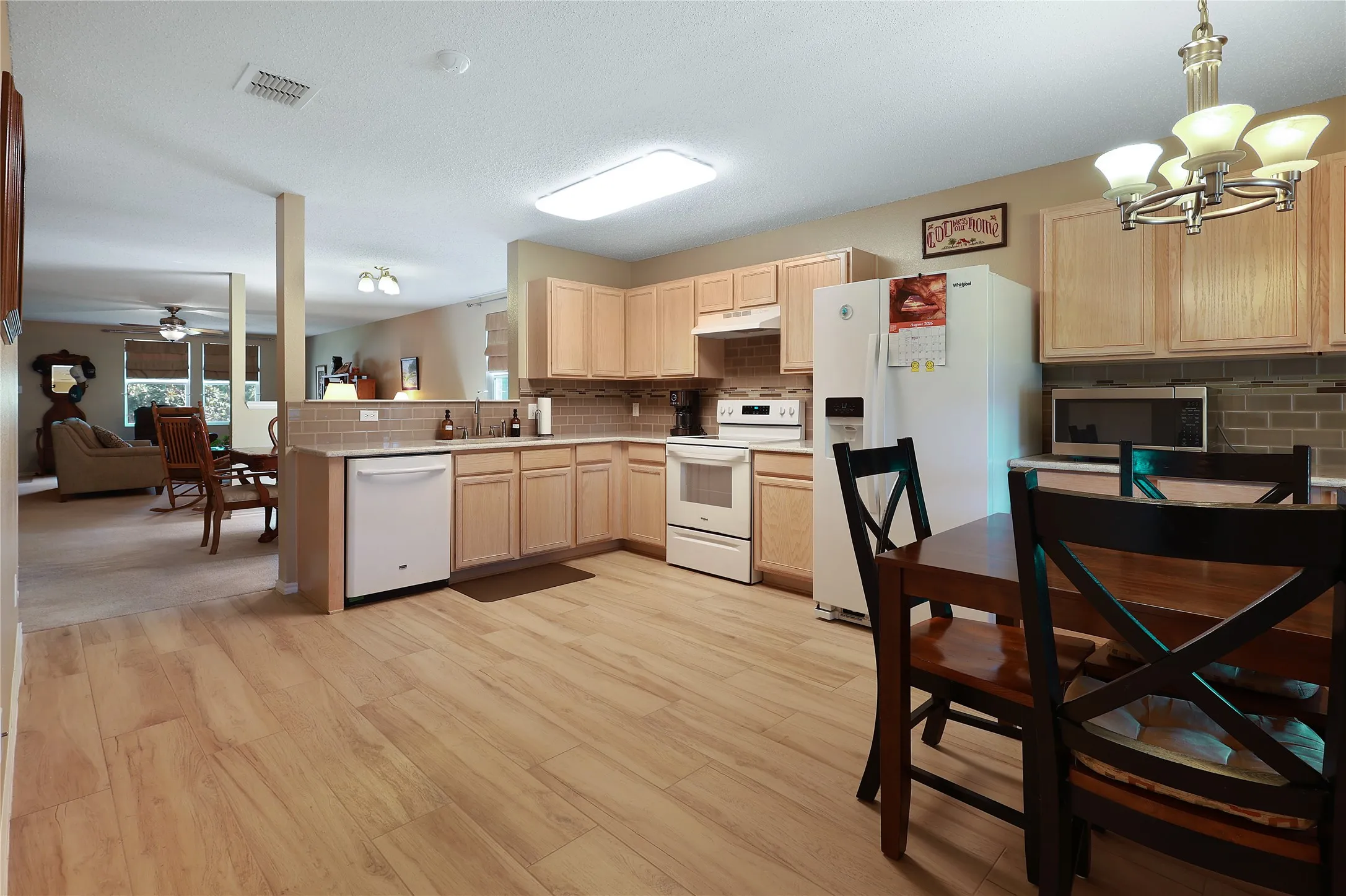 Kitchen featuring wood-finish flooring, light wood cabinetry, white appliances, and a tiled backsplash
