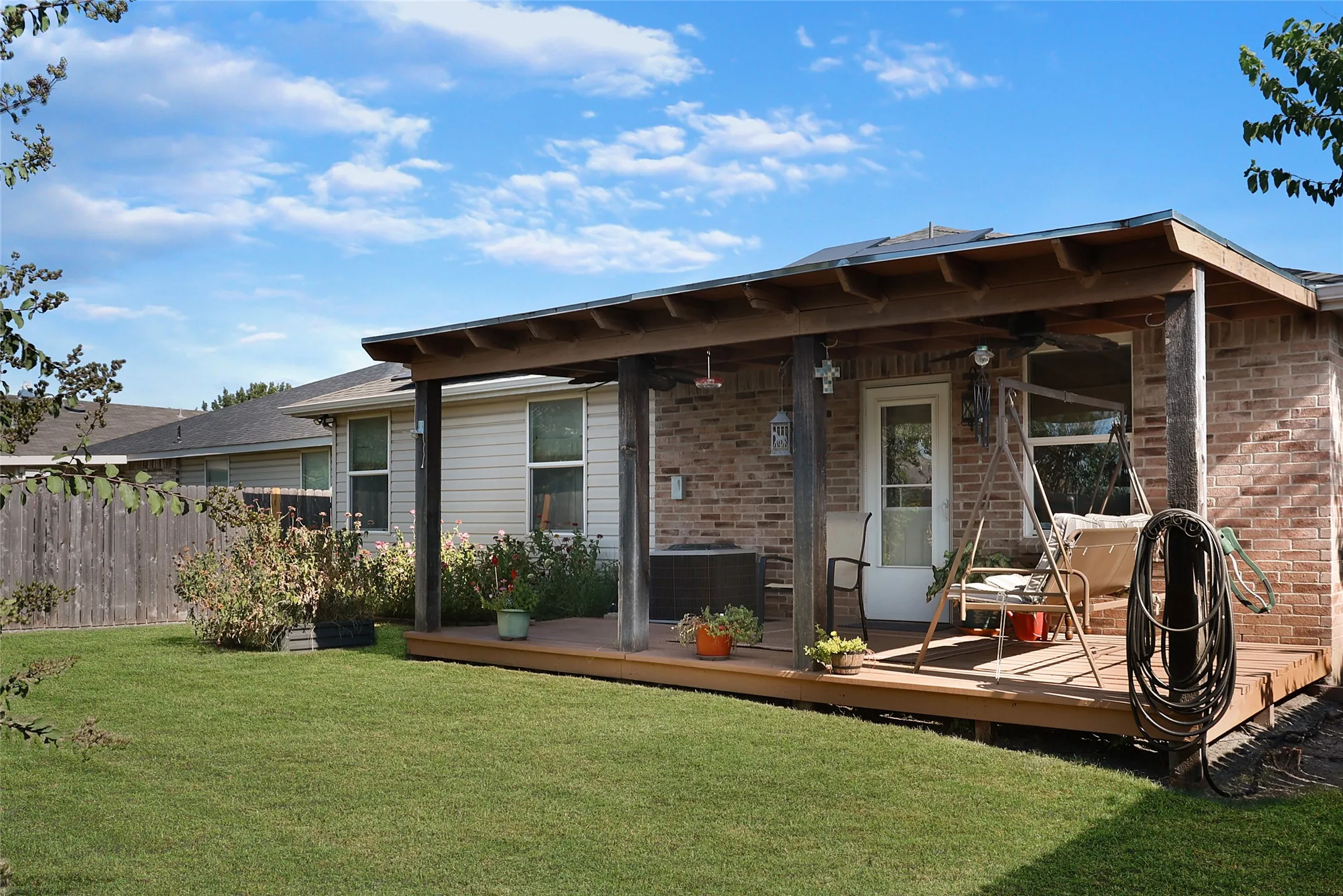 Expansive backyard featuring a green lawn, wood fence, and a covered wood deck