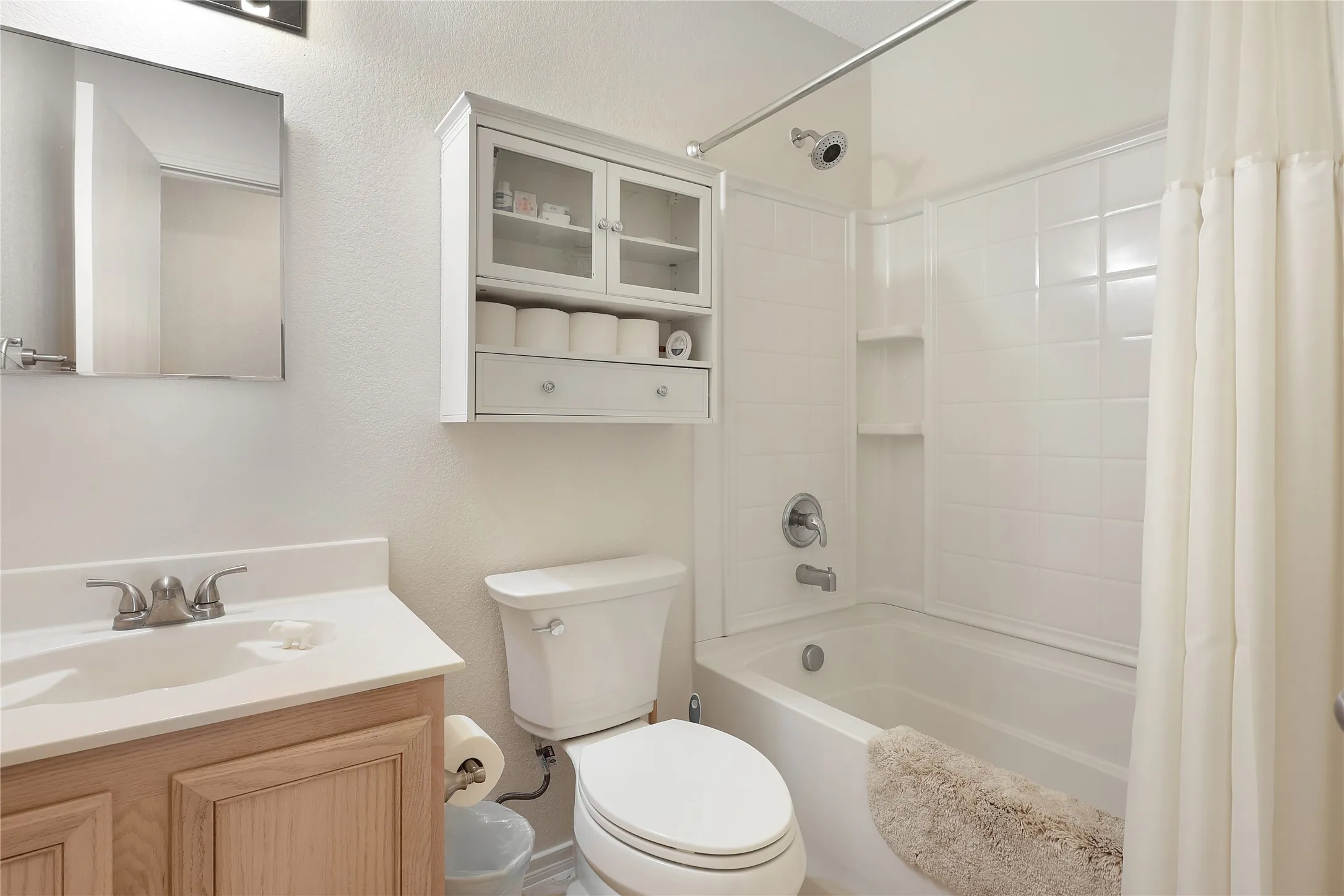 White vanity with a single basin sink, brushed nickel faucet, and wood-finish cabinetry