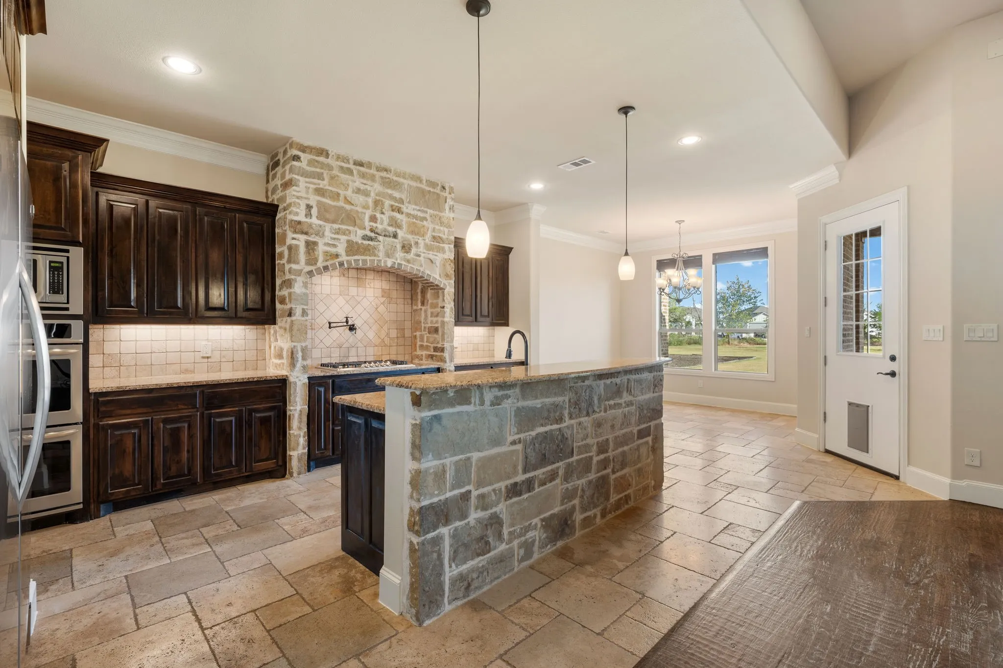 Kitchen featuring a stone-clad range hood, double wall ovens, built-in cabinetry, and a stone-clad island