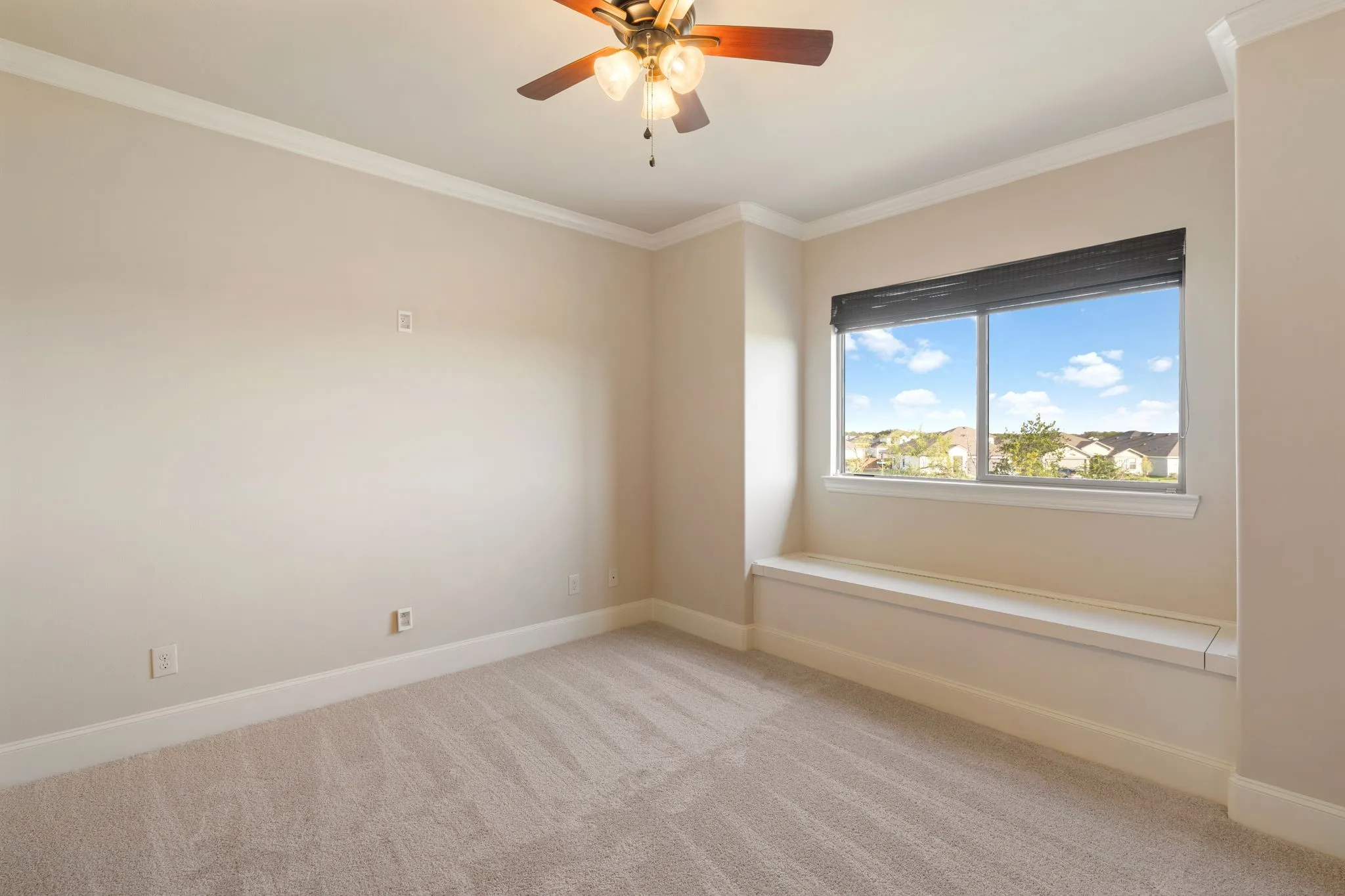 Plush carpeting, a built-in window bench, crown molding, and a ceiling fan with integrated lighting
