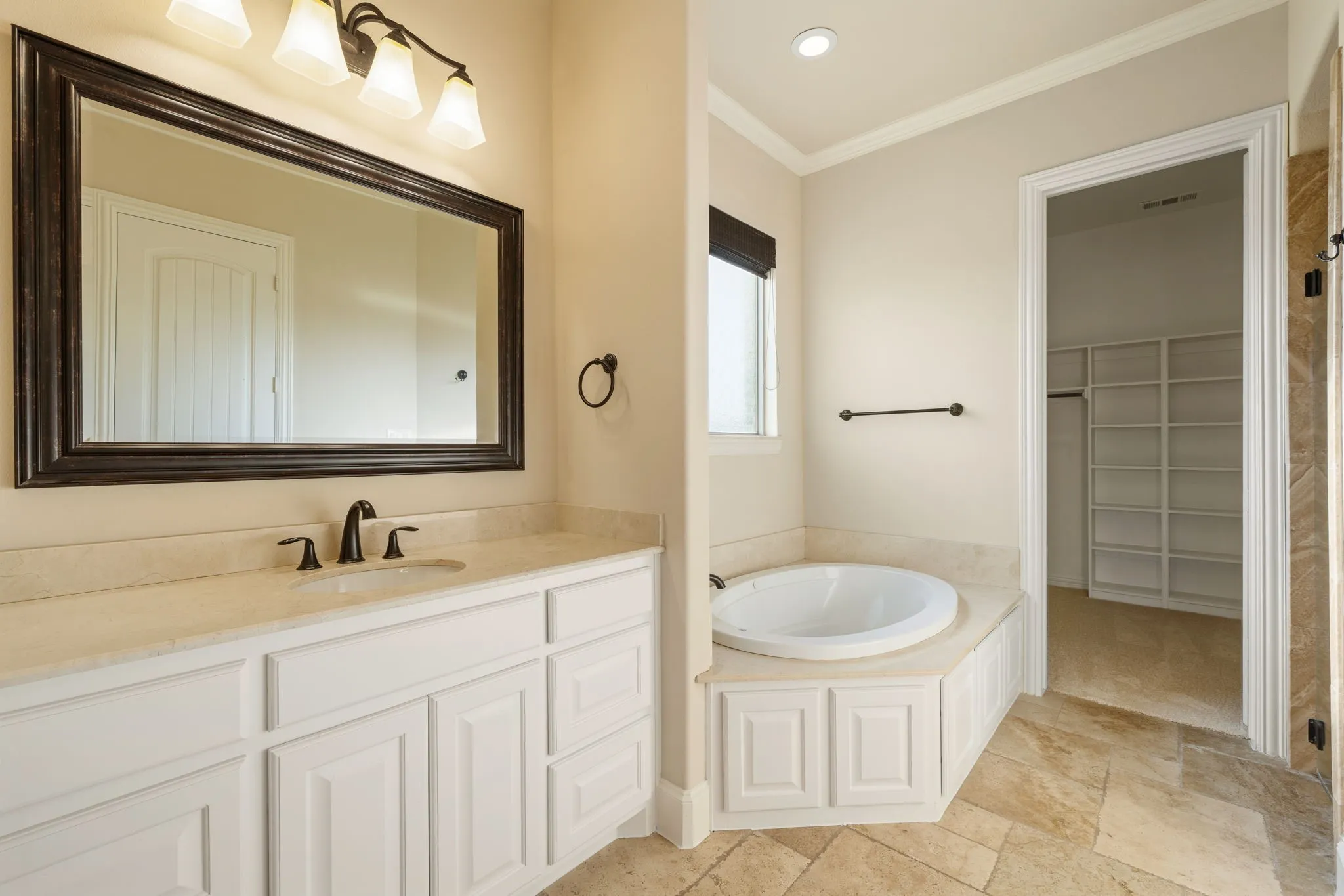 White vanity cabinetry with a light-toned countertop, a soaking tub, and a separate closet with built-in shelving