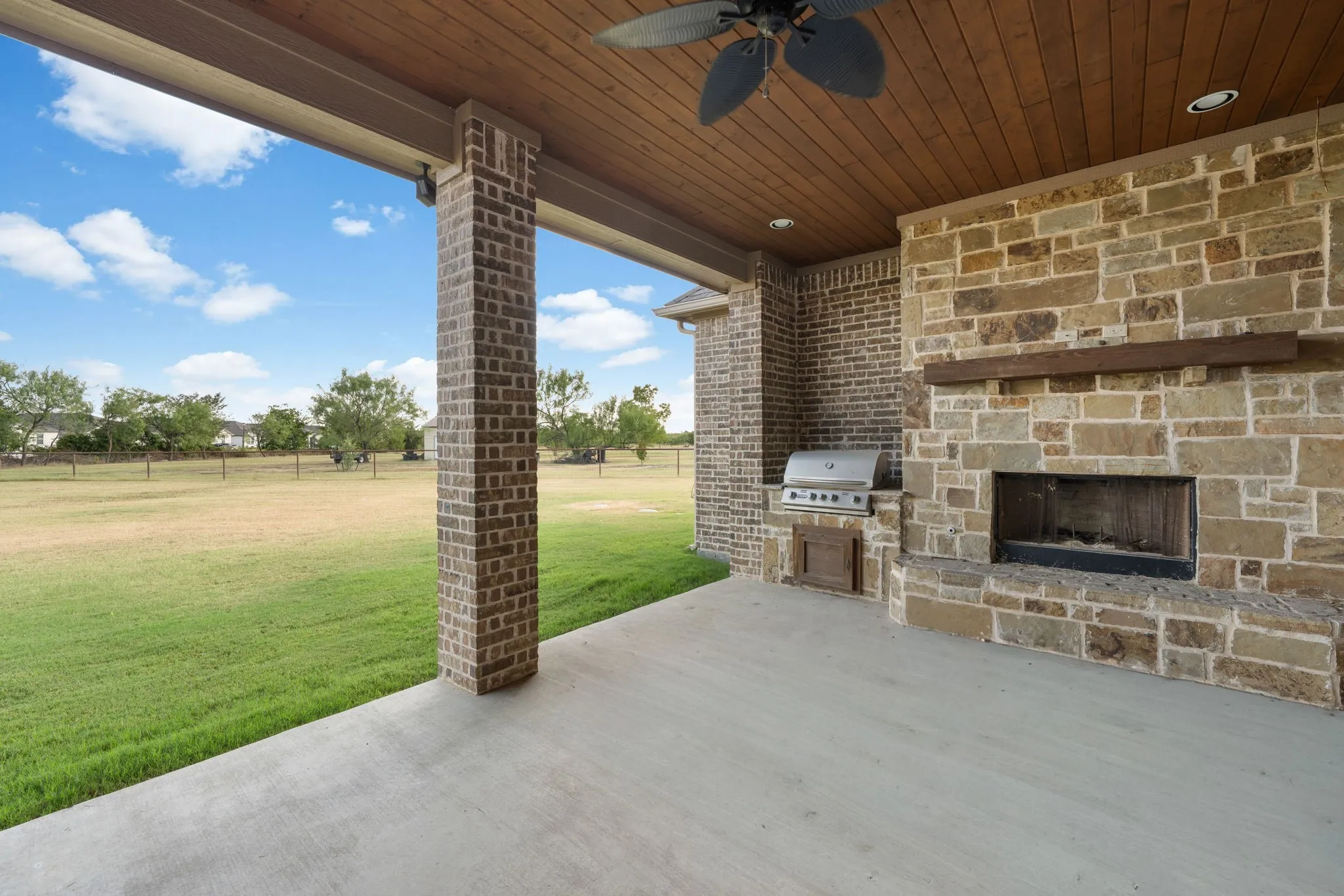 Covered patio featuring a wood-finish ceiling with a ceiling fan, a built-in stone fireplace with a wood mantel, a built-in grill, and brick columns