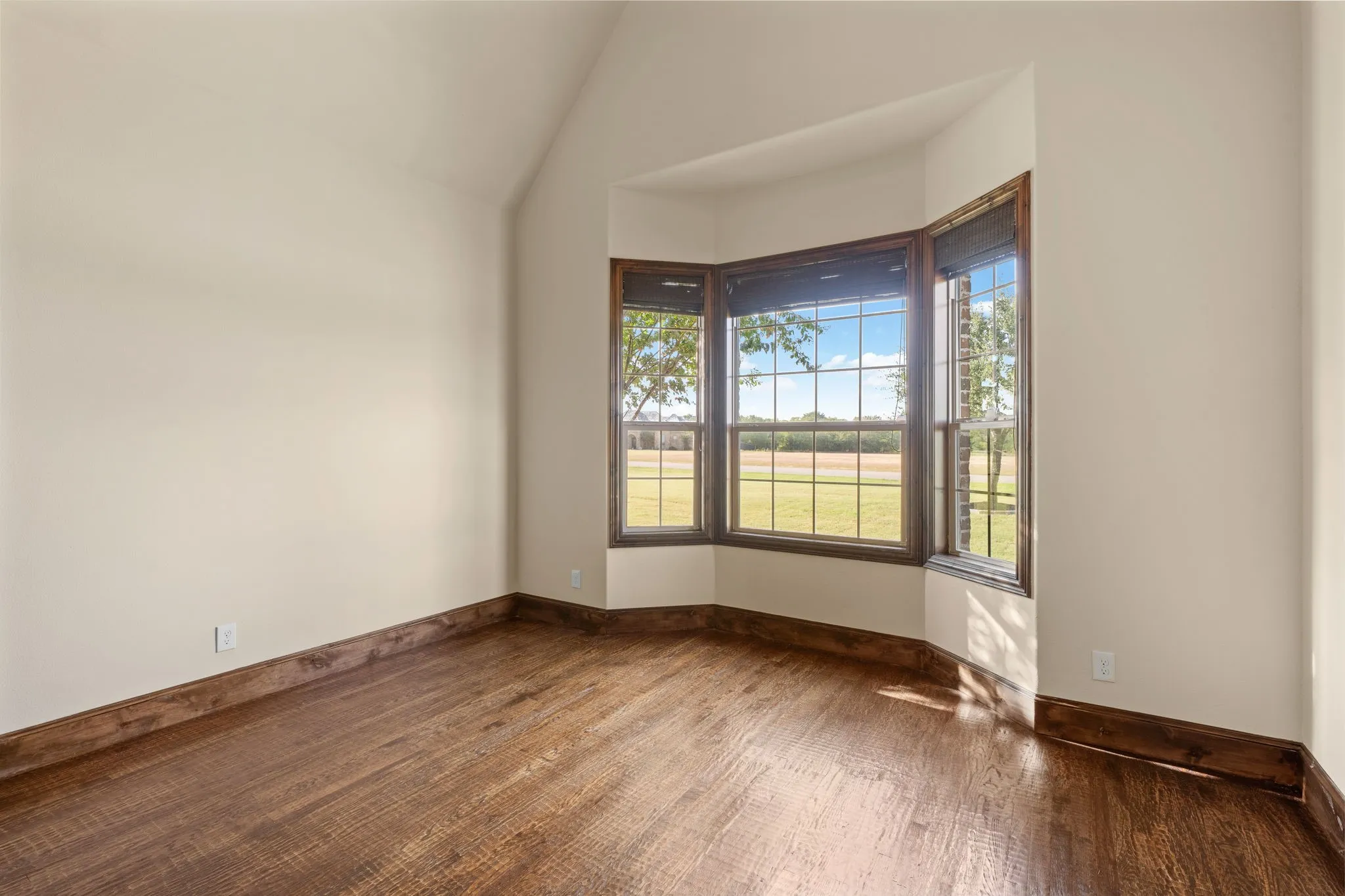 Expansive wood-finish flooring, a prominent bay window with dark wood trim, and a vaulted ceiling