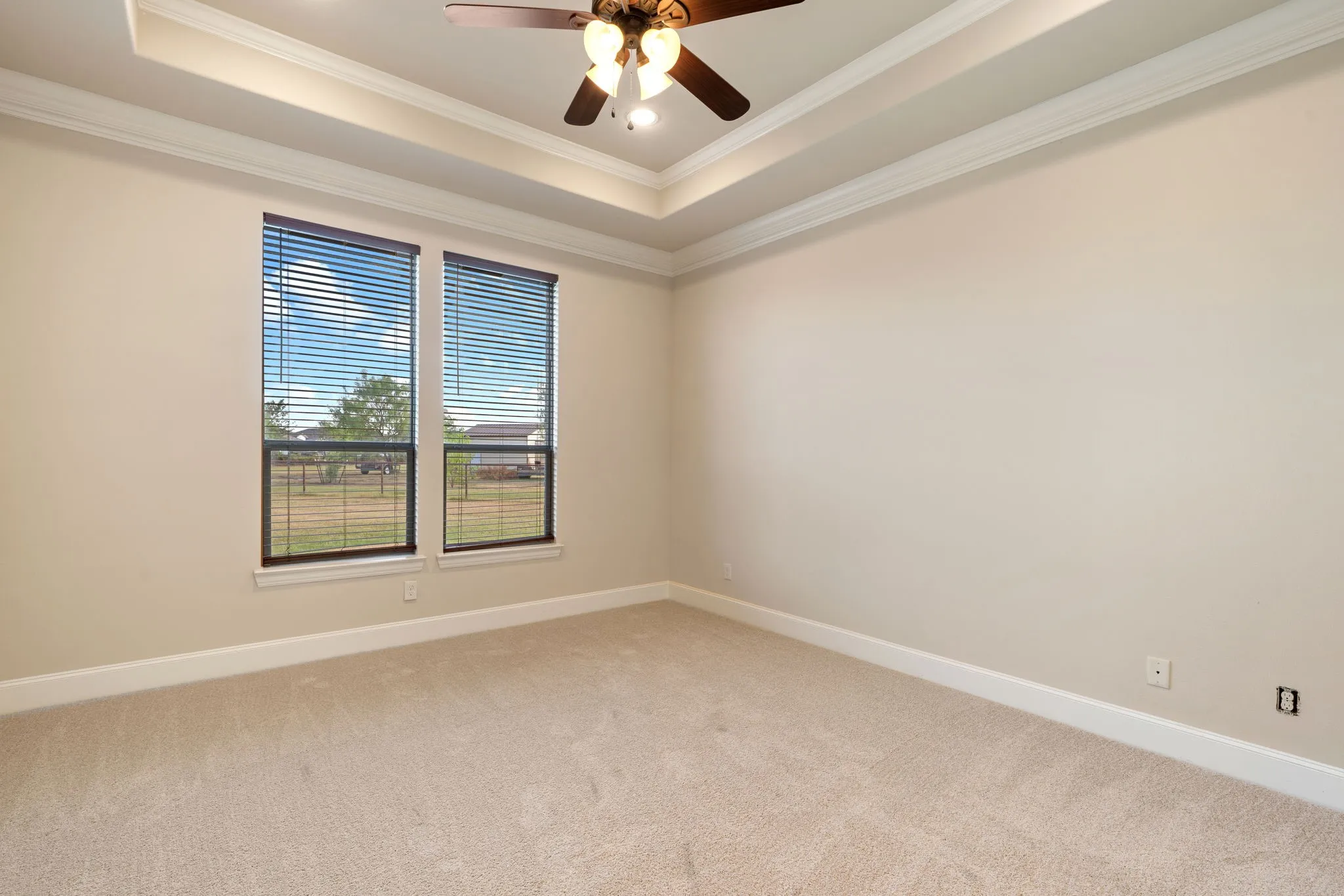 Tray ceiling with crown molding, ceiling fan with integrated lighting, recessed lighting, and two windows with blinds