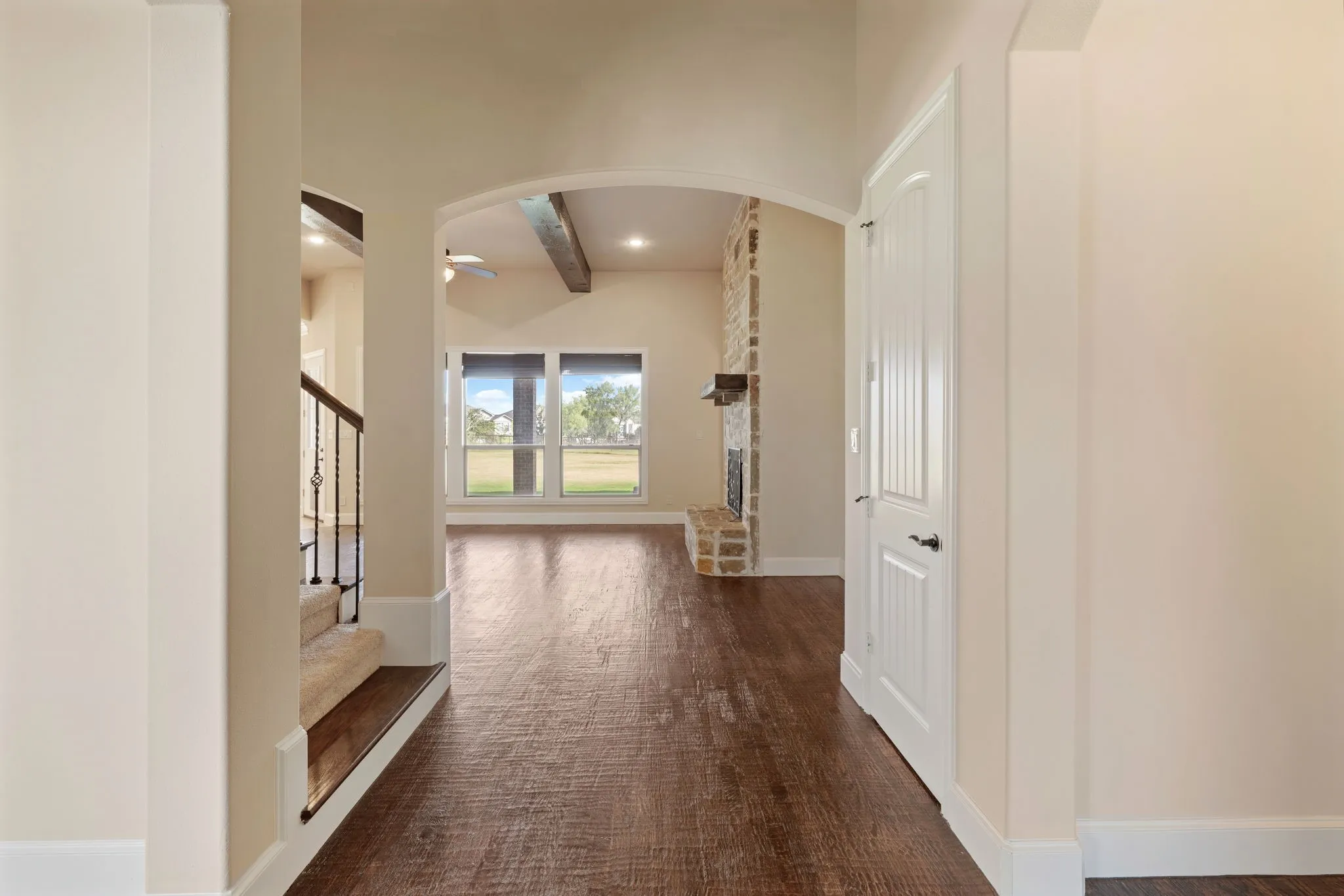 Arched entryway leading to a living area with wood-finish flooring, a stone fireplace, and exposed wood ceiling beams