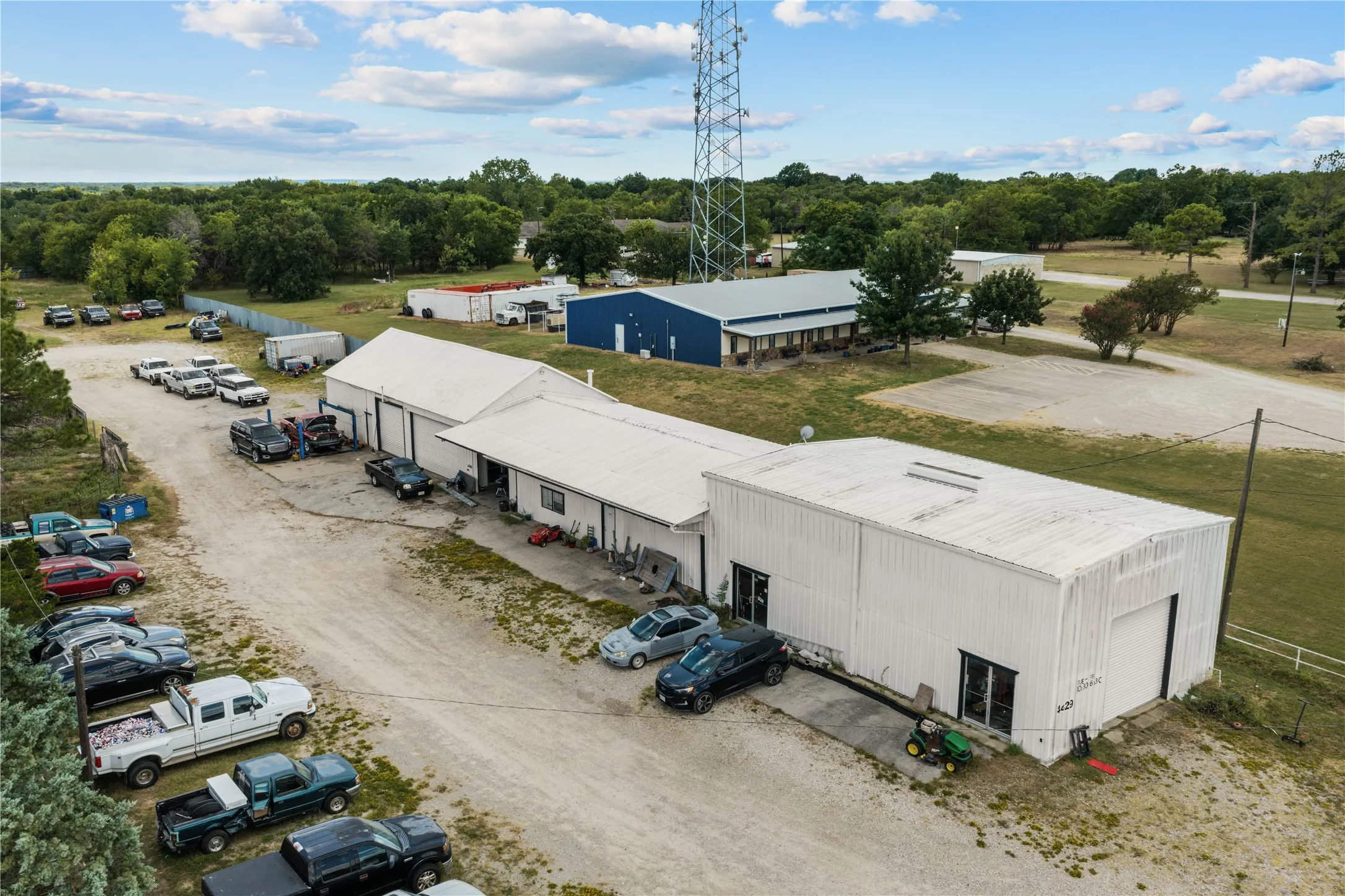 White metal-sided commercial structures with multiple bay doors and a gravel lot