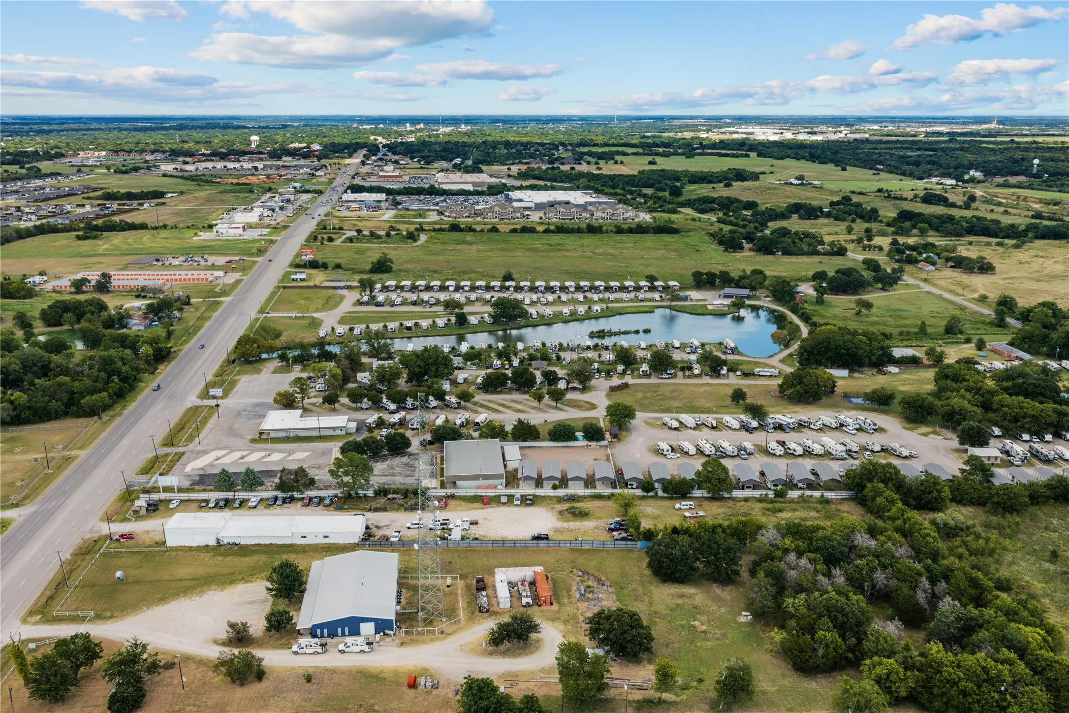 Aerial perspective showcasing a large commercial structure with a blue roof, surrounding paved areas, and an adjacent open field