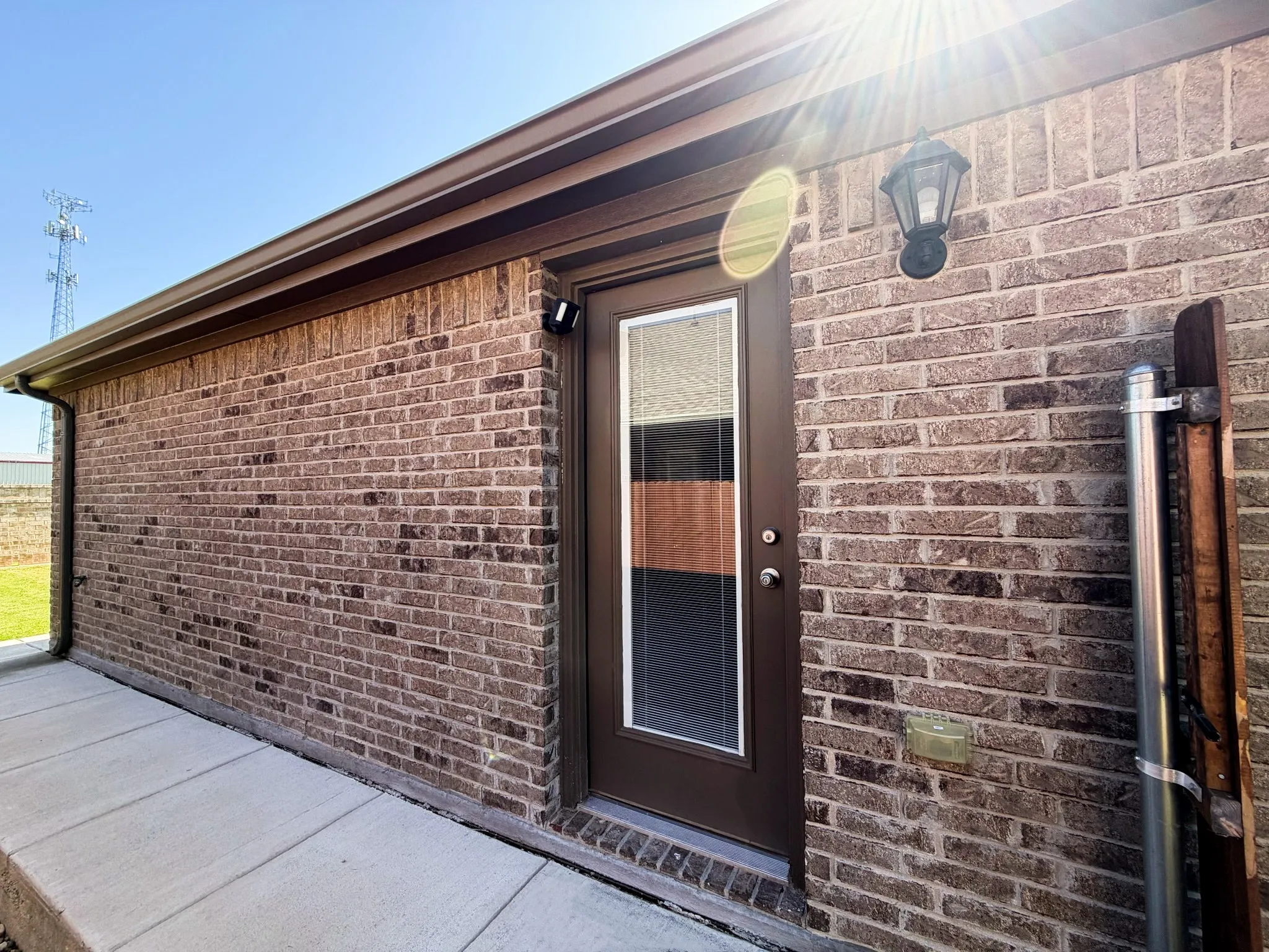 Brick exterior with a brown trim door, exterior lighting, and a concrete pathway