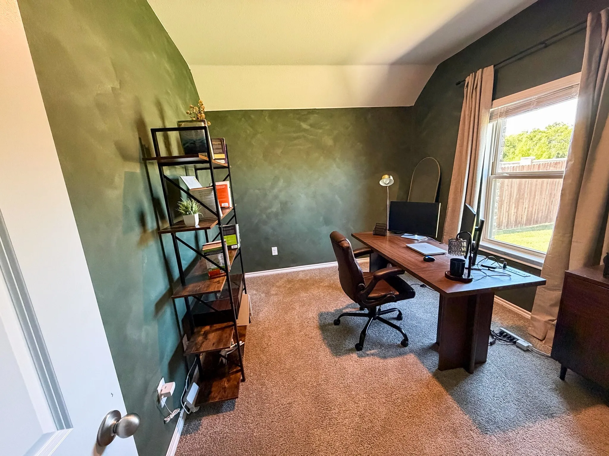Dedicated home office featuring textured accent wall, cork flooring, large windows with natural light, built-in desk workspace, and ample storage shelving
