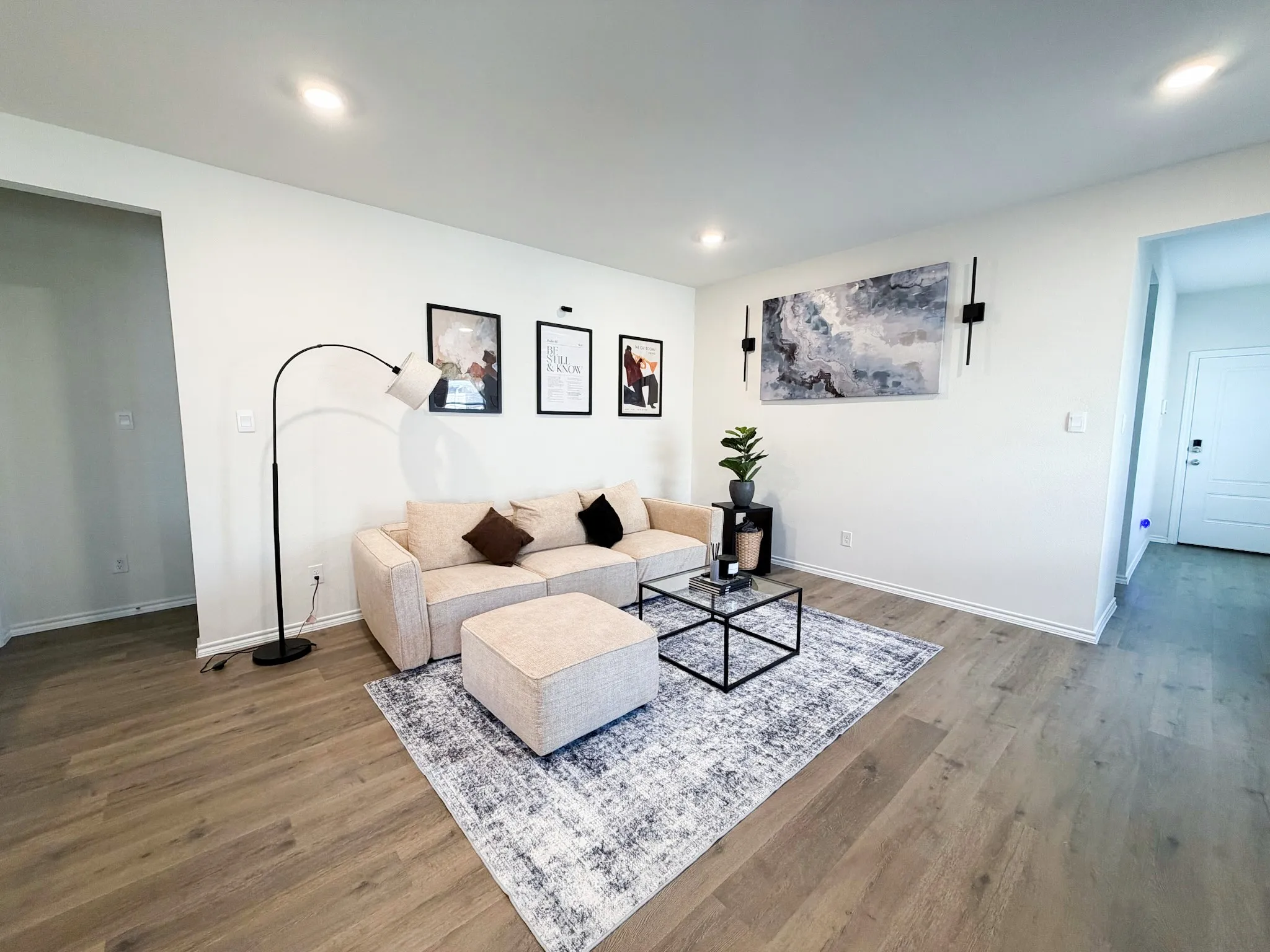 Modern living room featuring warm wood-finish flooring, recessed ceiling lighting, and clean white walls