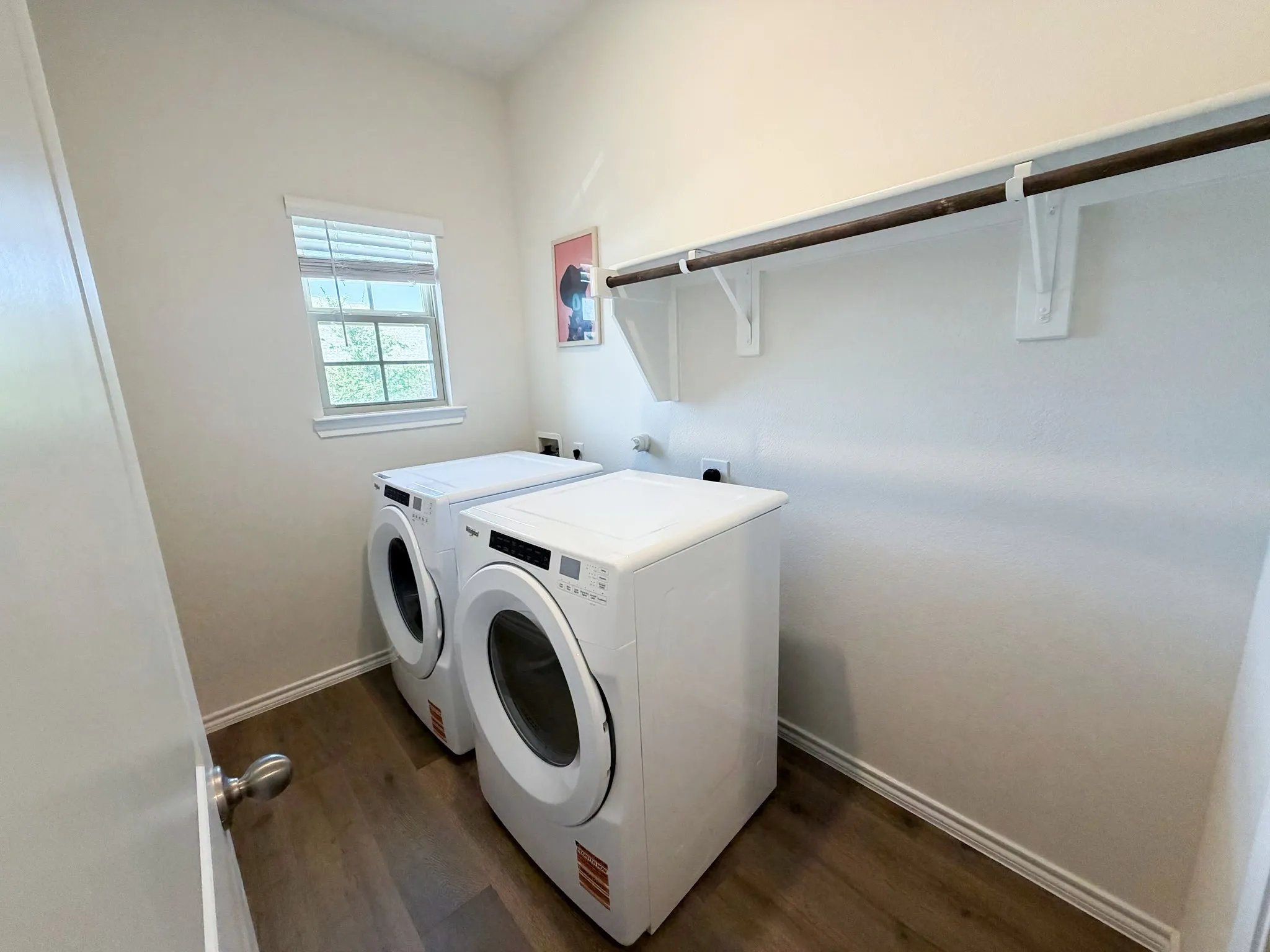 Window with white trim, wood-finish flooring, white walls, and a built-in shelving and hanging rod system