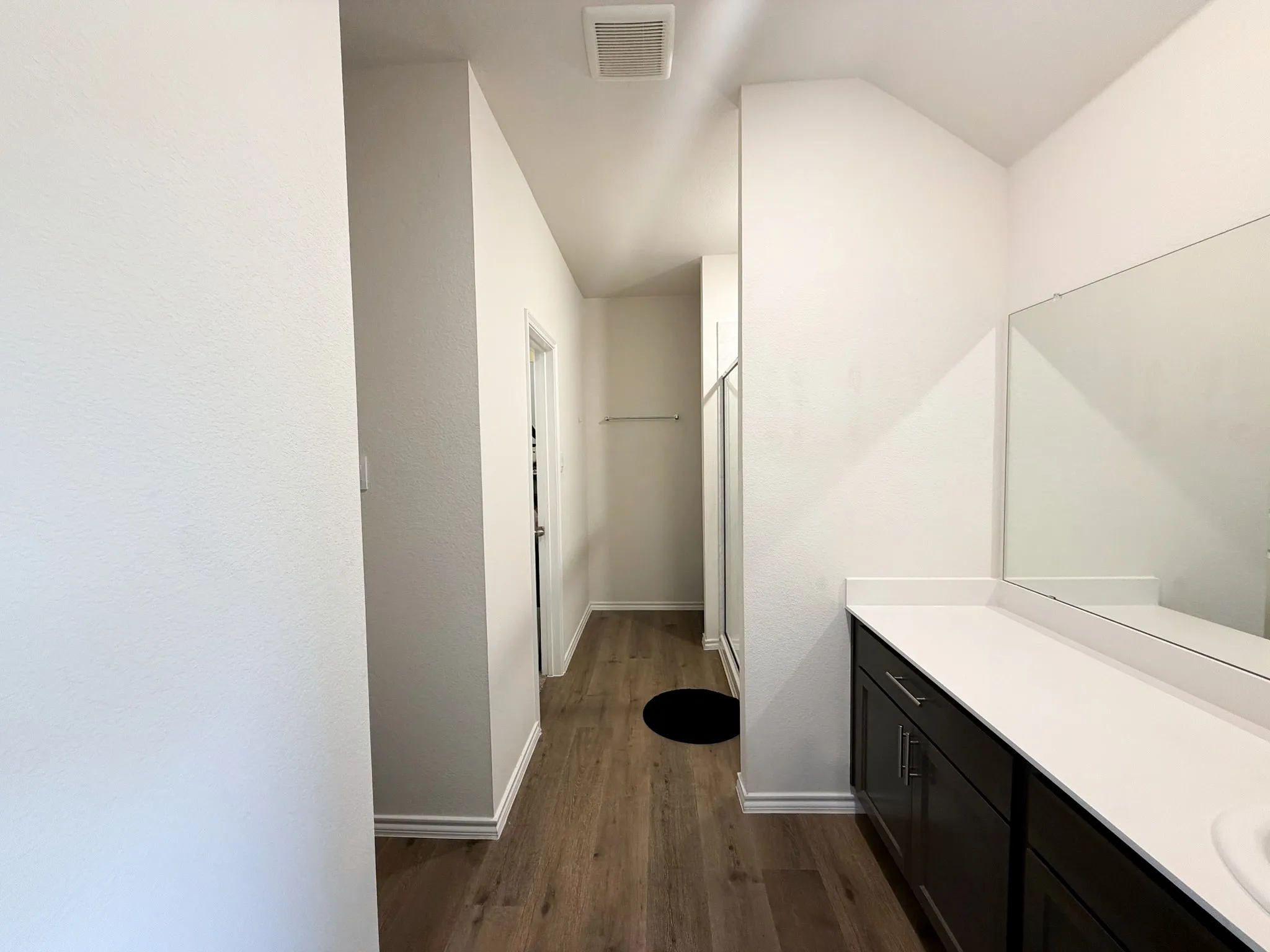 Wood-finish flooring, white walls, built-in vanity with dark cabinetry, integrated rectangular sink, and a large wall-mounted mirror
