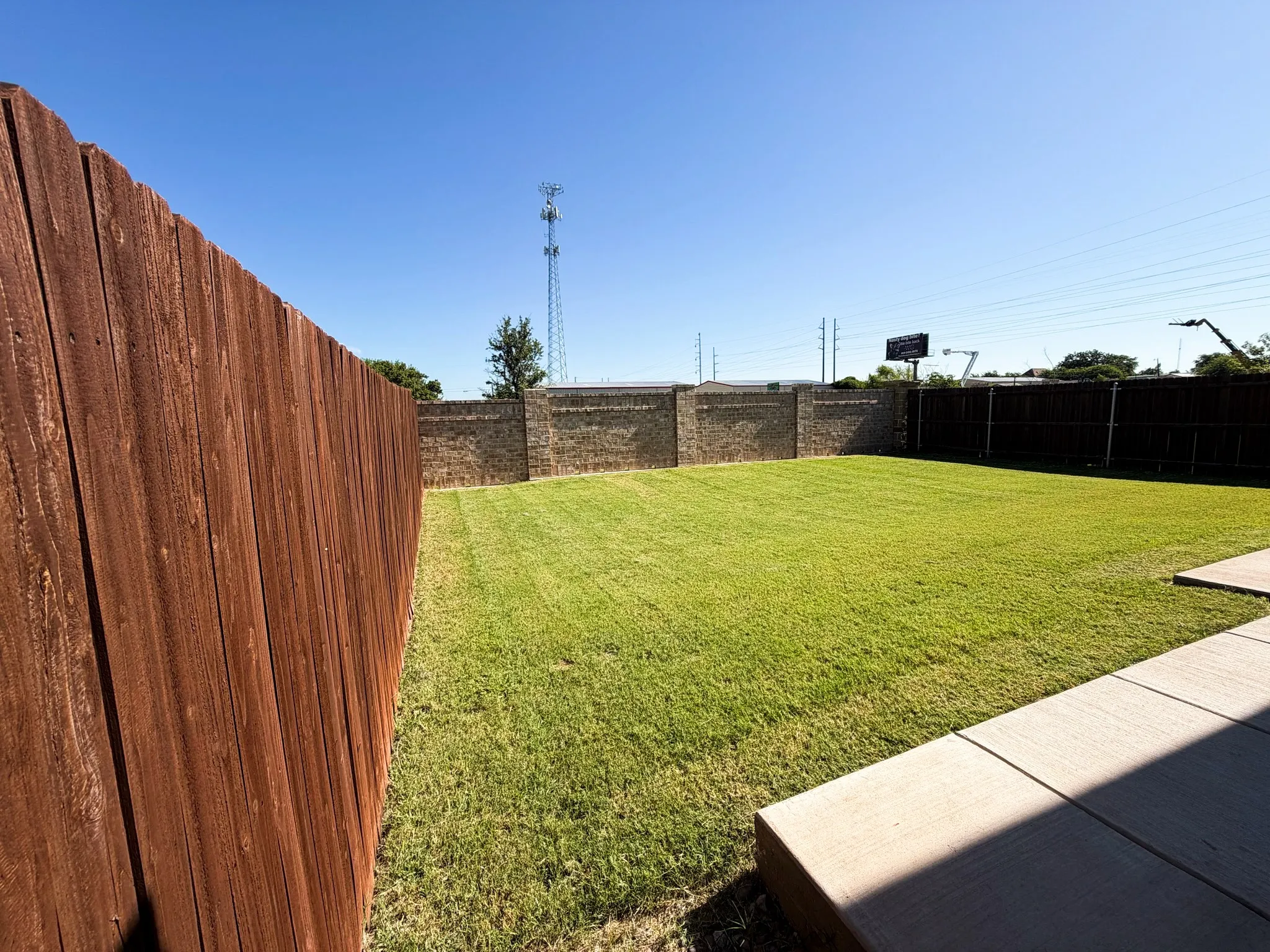 Expansive grassy yard with concrete patio, wood fencing, and brick perimeter wall
