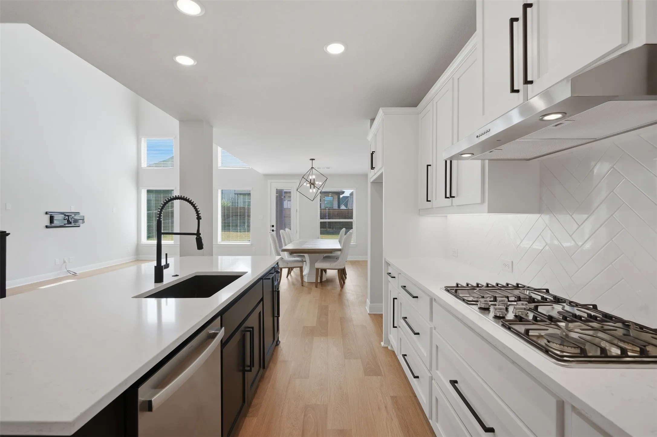 Modern kitchen featuring crisp white cabinetry, light-toned wood-finish flooring, recessed lighting, and a gas range complemented by a sleek stainless steel vent hood