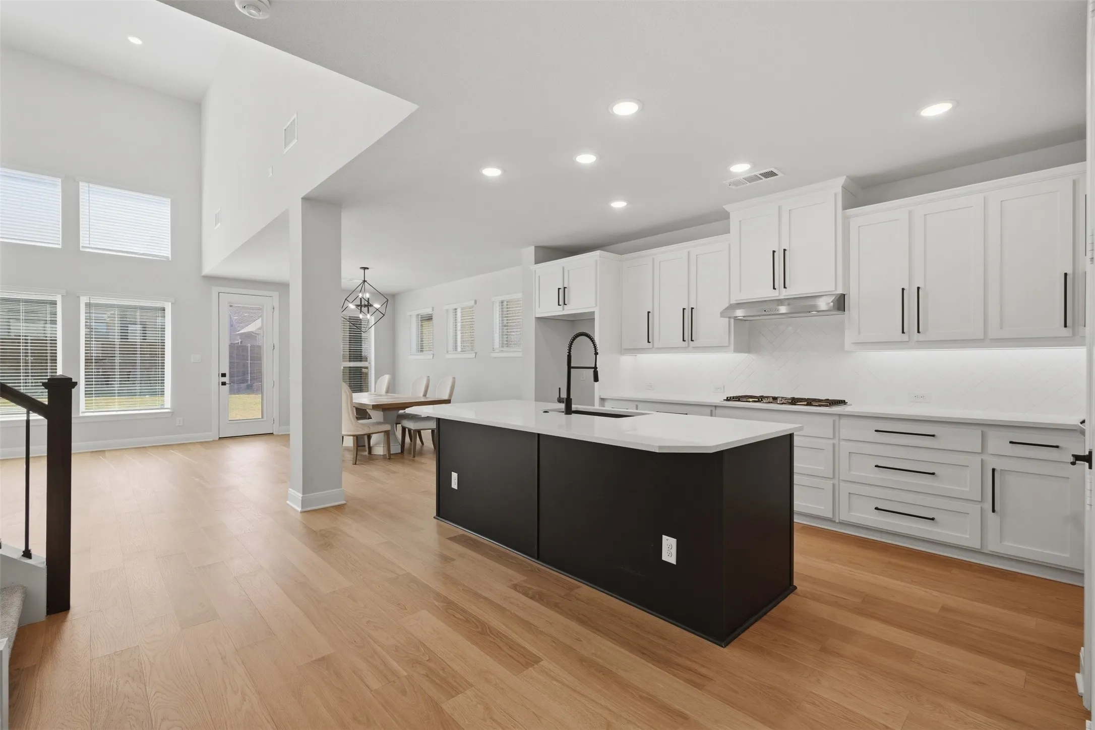 Open-concept living space featuring wood-finish flooring, a kitchen with white cabinetry and a dark island, stainless steel range hood, and recessed lighting