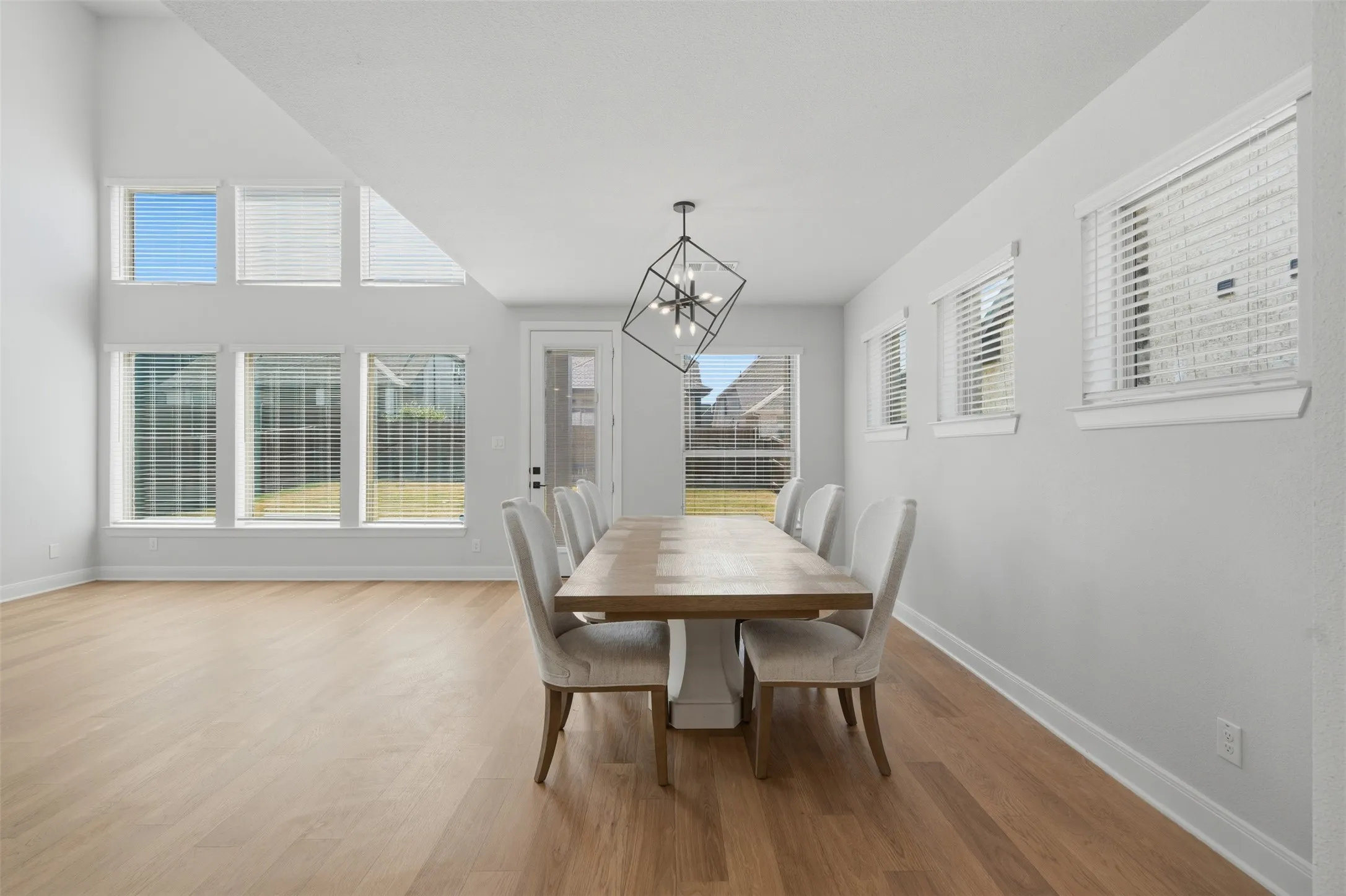 Bright, open-concept living space featuring wood-look flooring, crisp white cabinetry, a contrasting dark island, stainless steel range hood, and recessed lighting