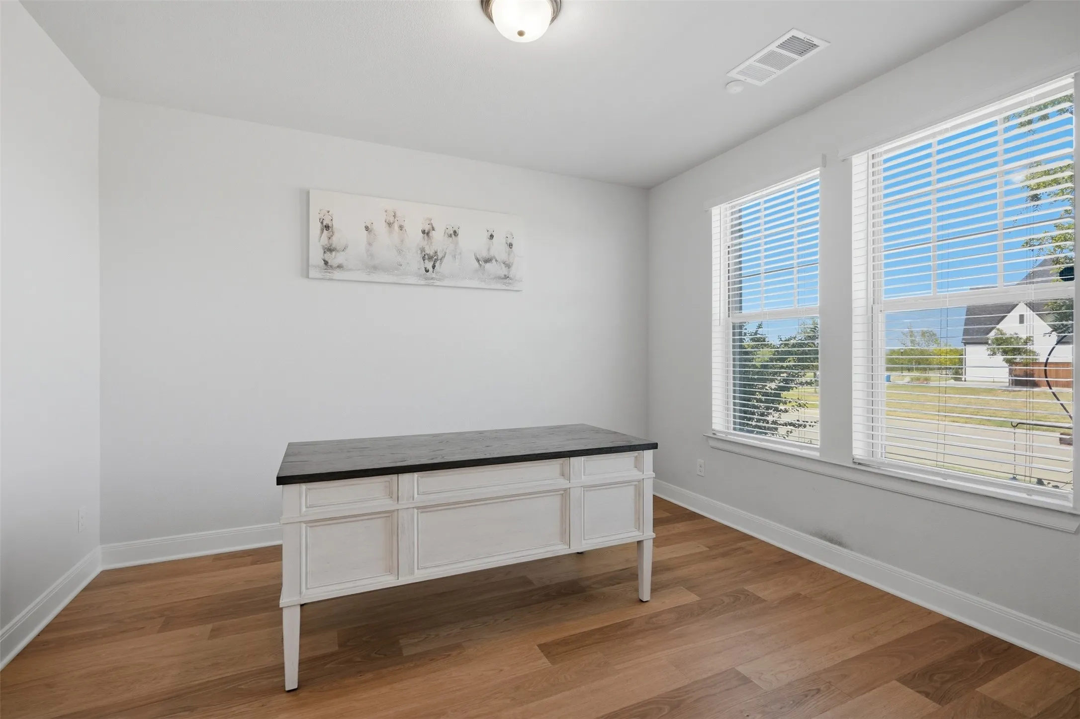 Bright and inviting home office featuring wood-finish flooring and expansive windows that fill the space with natural light, creating an ideal setting for work, study, or productivity