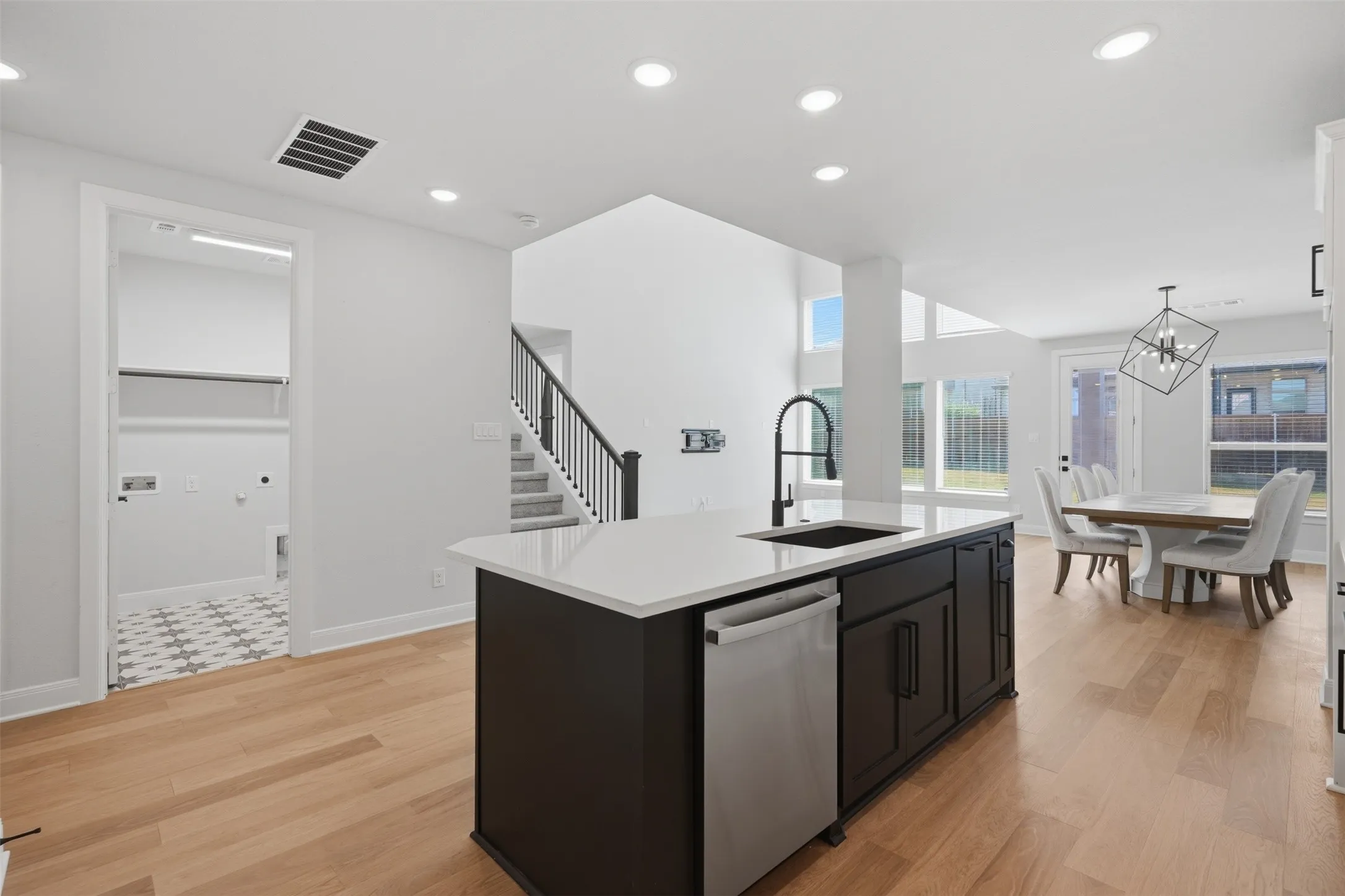 Open-concept kitchen featuring a striking dark-toned island with crisp white countertops, an integrated sink, and stainless steel dishwasher, blending modern style with everyday functionality