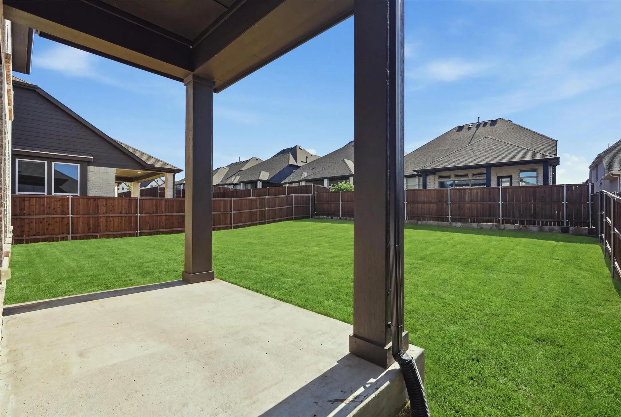 Inviting covered outdoor patio with a durable concrete surface, expansive lawn, and wood privacy fencing, creating a comfortable setting for outdoor dining, relaxation, and entertaining