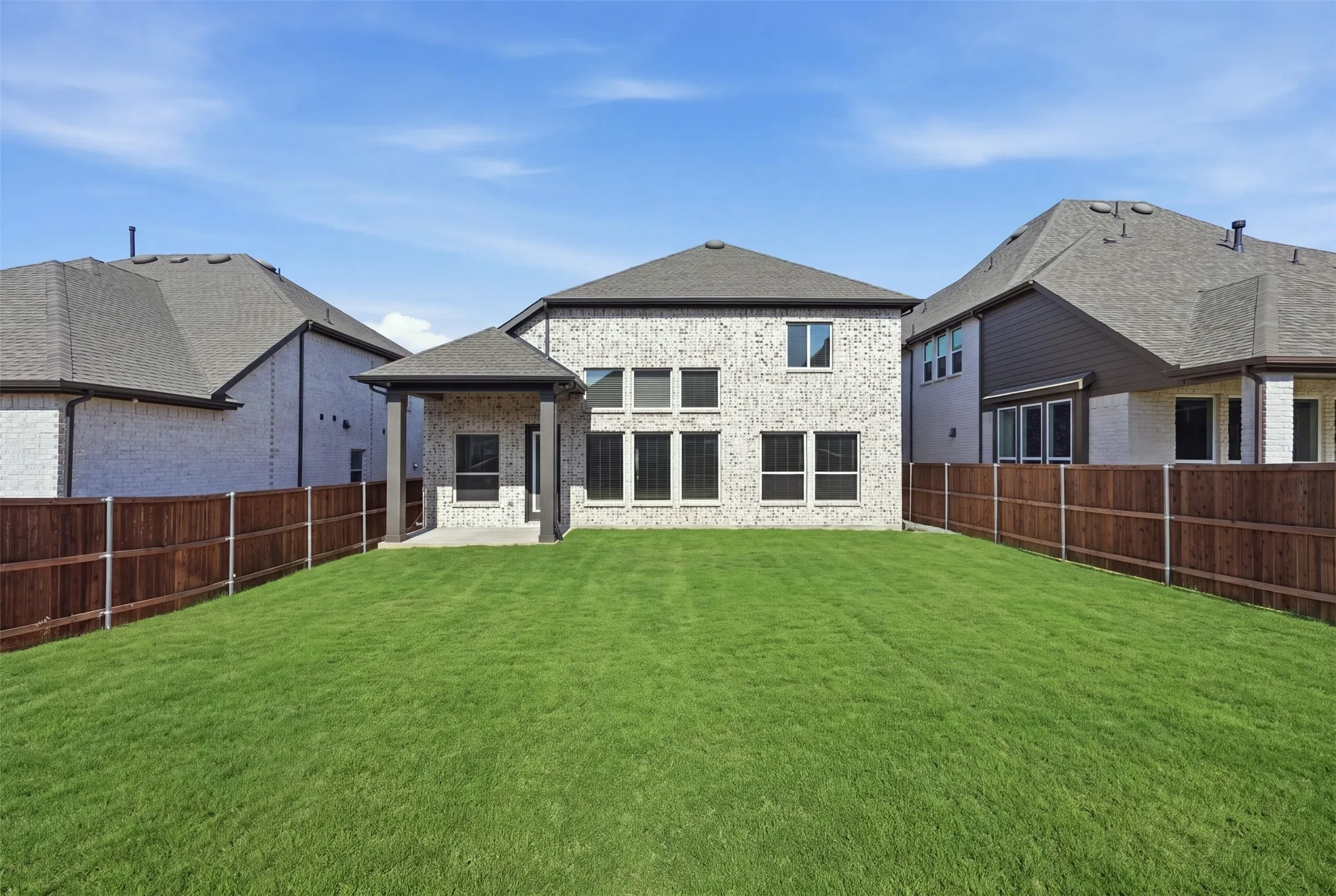 Expansive green lawn complemented by a covered patio, full privacy fencing, and multiple windows overlooking the outdoor space, creating a private and inviting setting for relaxation and entertaining