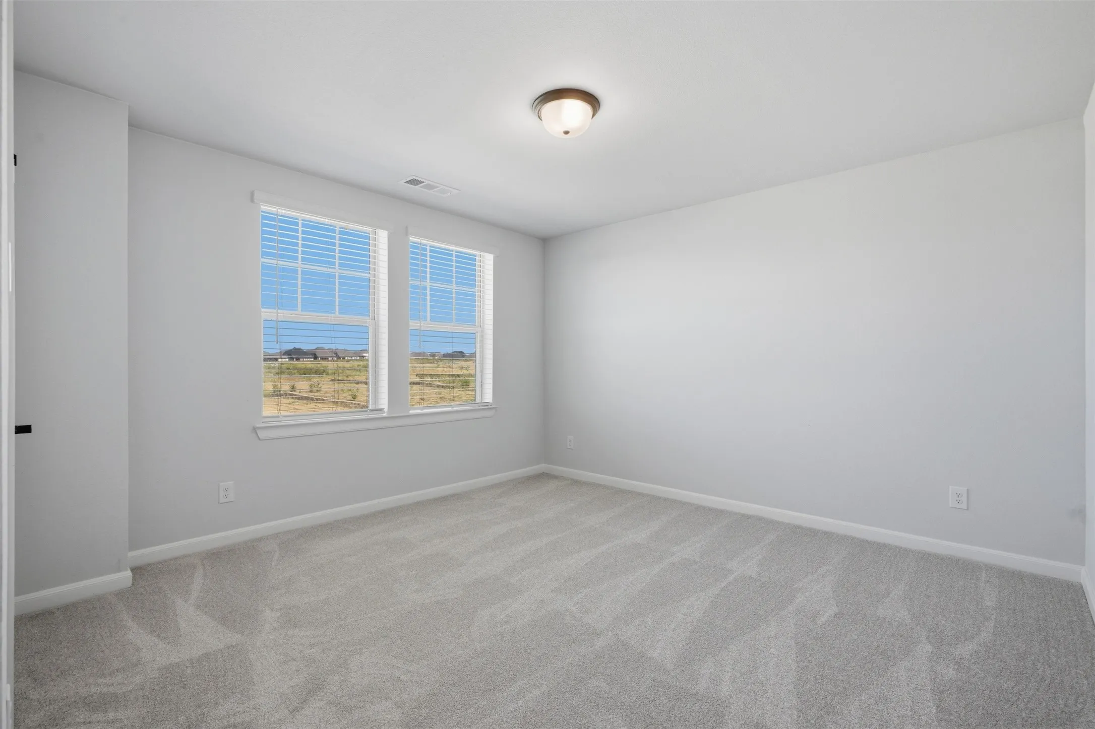 Well-appointed bedroom featuring neutral wall tones, plush wall-to-wall carpeting, two windows with blinds, and a ceiling-mounted light fixture, creating a bright and comfortable retreat