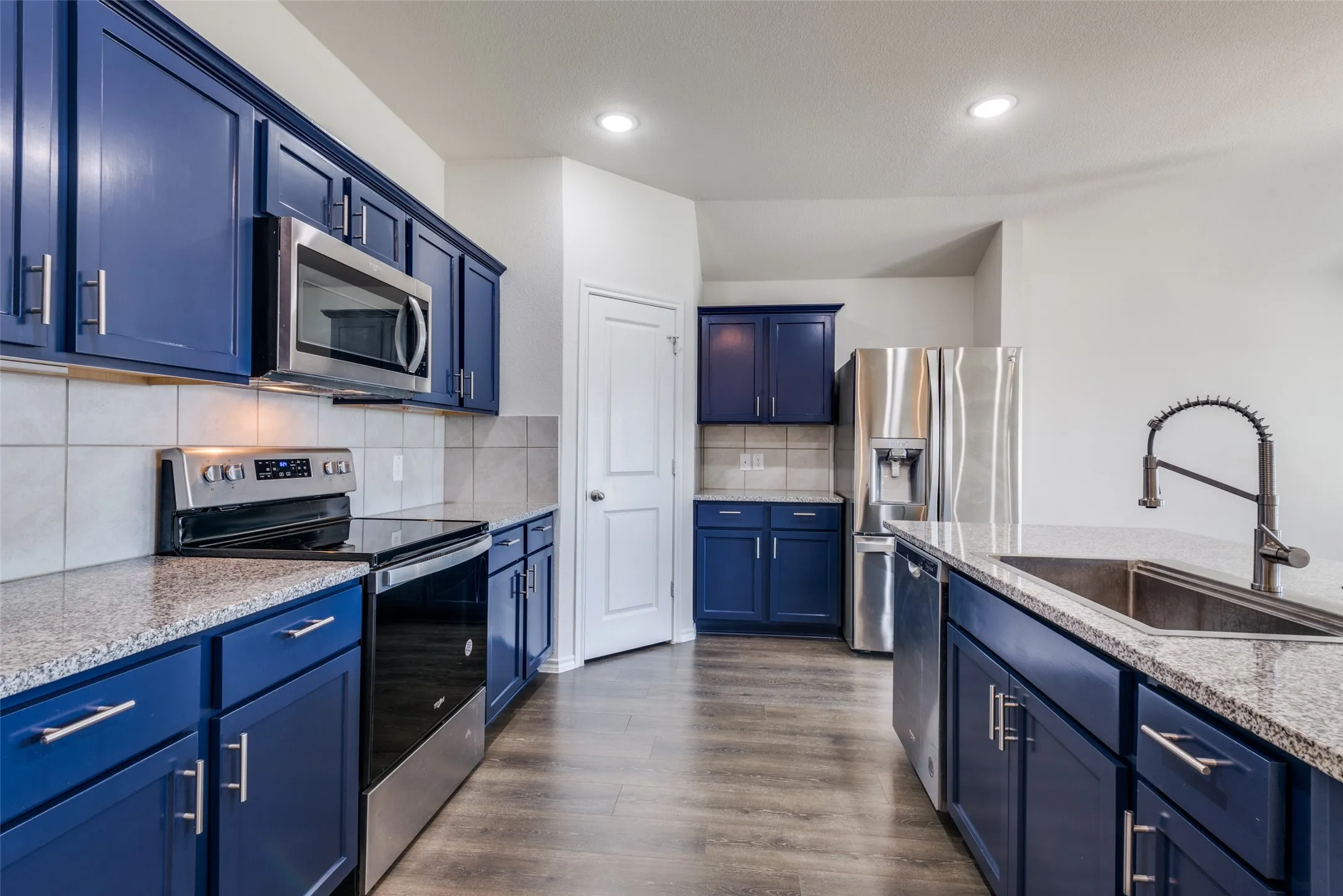 Kitchen featuring blue cabinetry, stainless steel appliances, granite countertops, tile backsplash, and wood-finish flooring