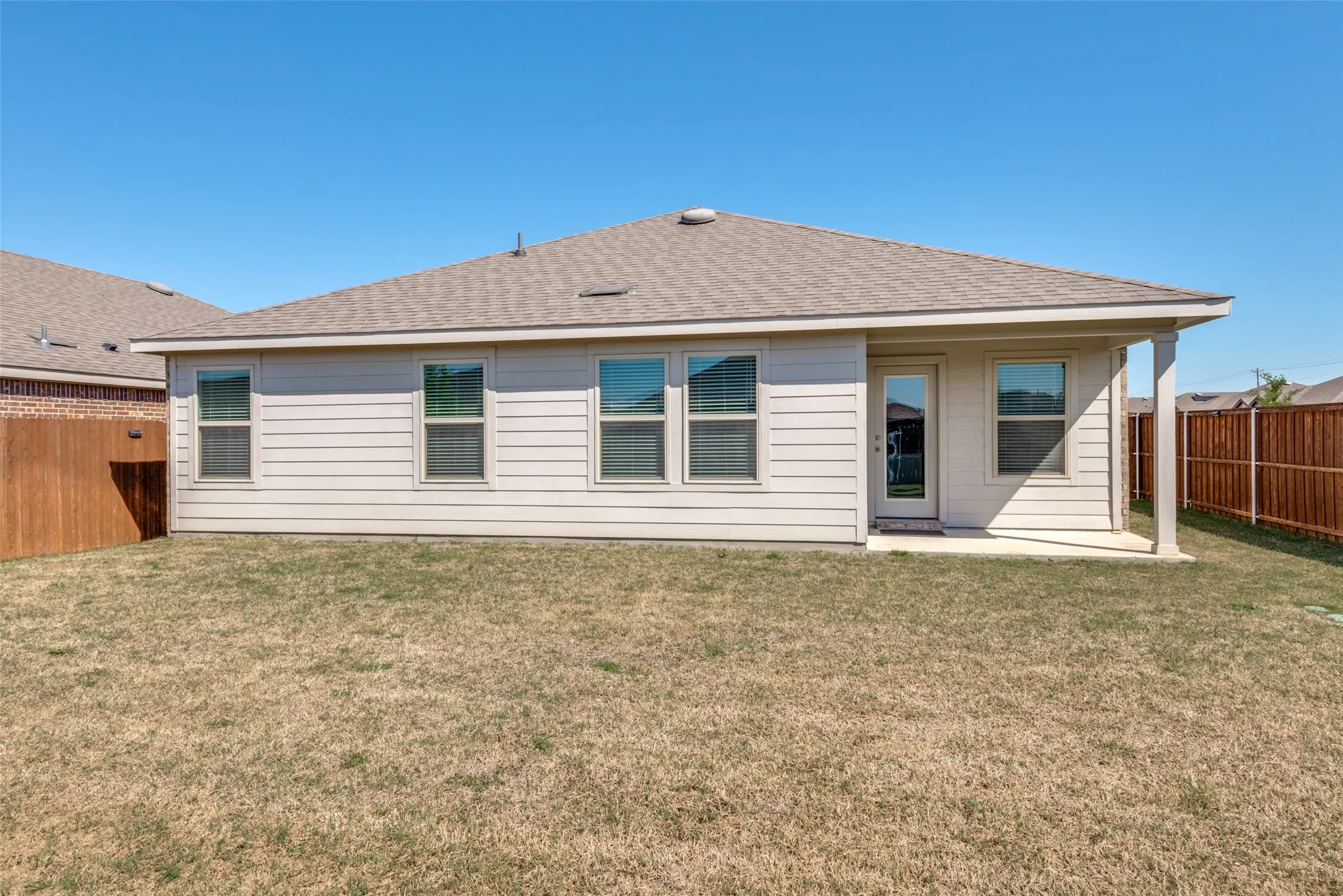 Rear exterior featuring a covered patio, multiple windows, and a wood privacy fence