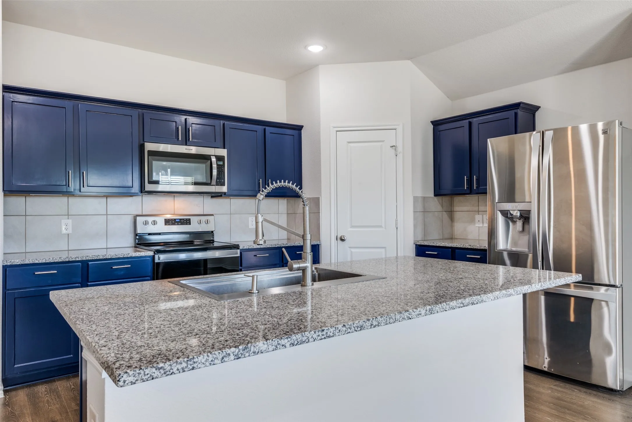 Kitchen featuring an island with a stainless steel undermount sink and a high-arc faucet, blue cabinetry with stainless steel hardware, stainless steel appliances, and tile backsplash