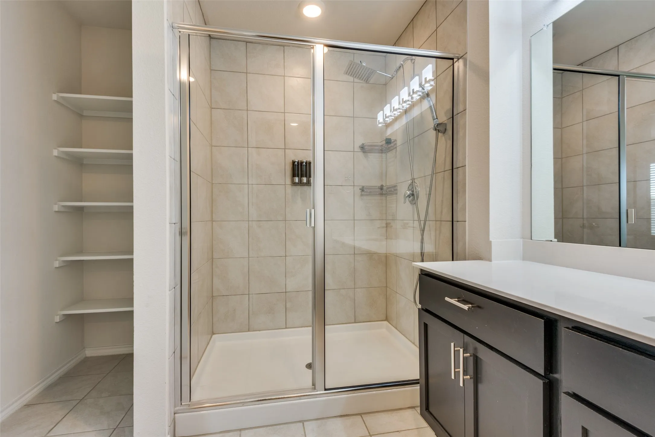 Glass-enclosed shower with tile surround, rain shower head, and built-in shelving