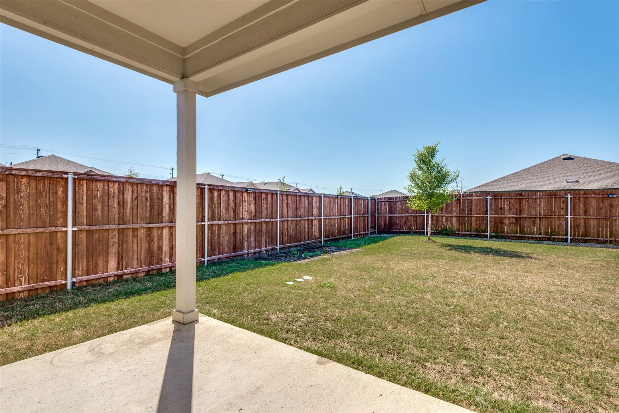 Expansive backyard featuring a concrete patio, wood privacy fencing, and a mature tree