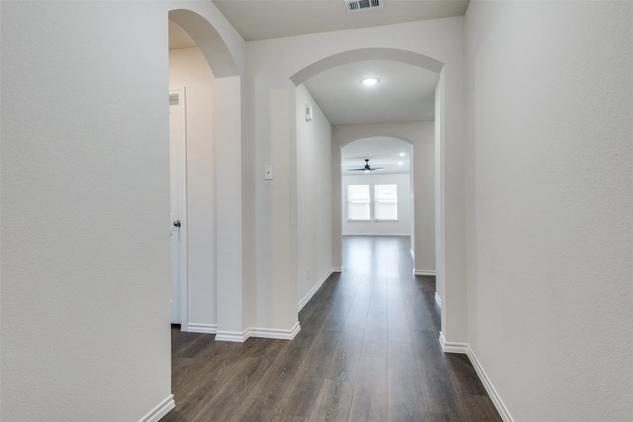 Hallway featuring wood-finish flooring, arched doorways, white trim, and recessed lighting