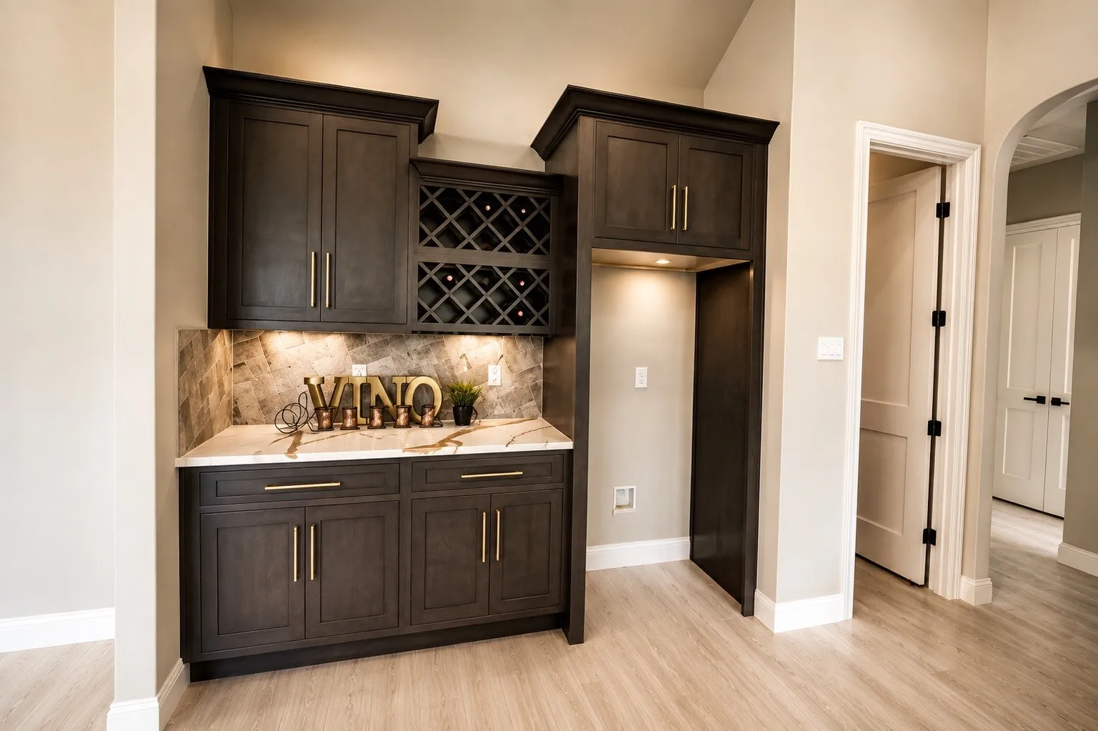 Built-in cabinetry with crown molding, wine rack, under-cabinet lighting, light-toned countertop, and backsplash