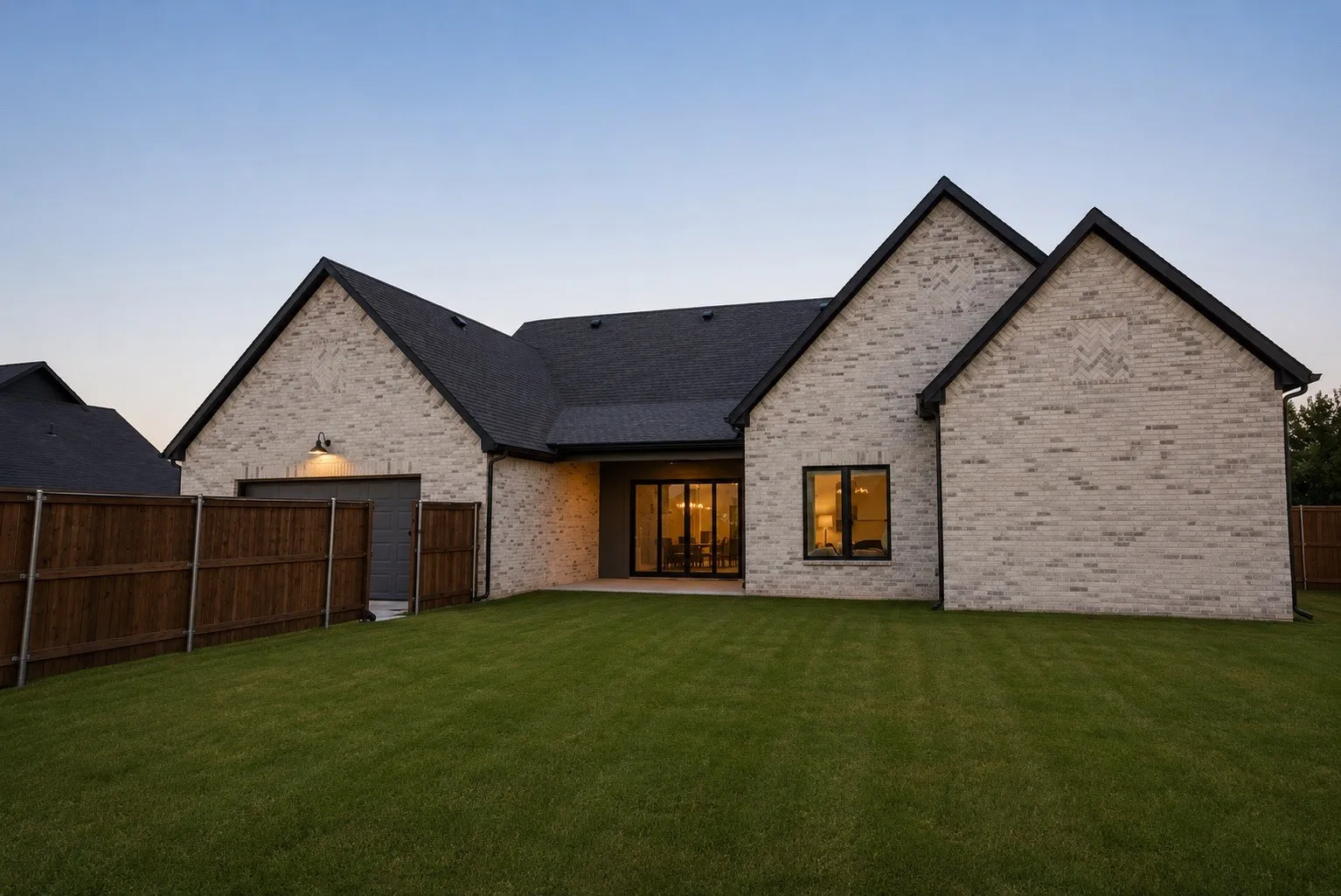 Spacious backyard featuring a manicured lawn, full privacy fencing, and a light brick exterior with black trim