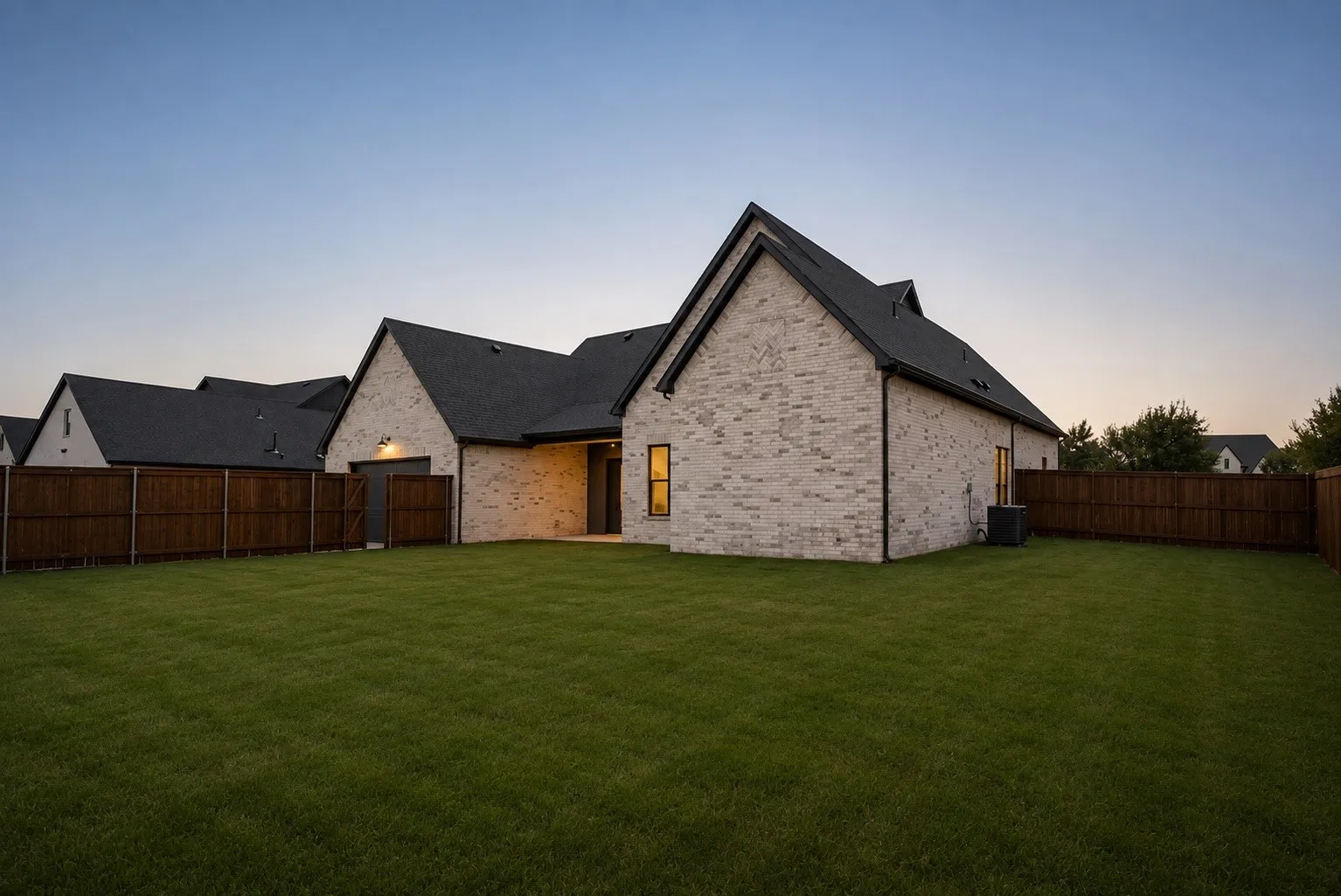 Expansive grassy yard with a dark wood fence surrounding a brick exterior home featuring gabled roofs and an outdoor light fixture