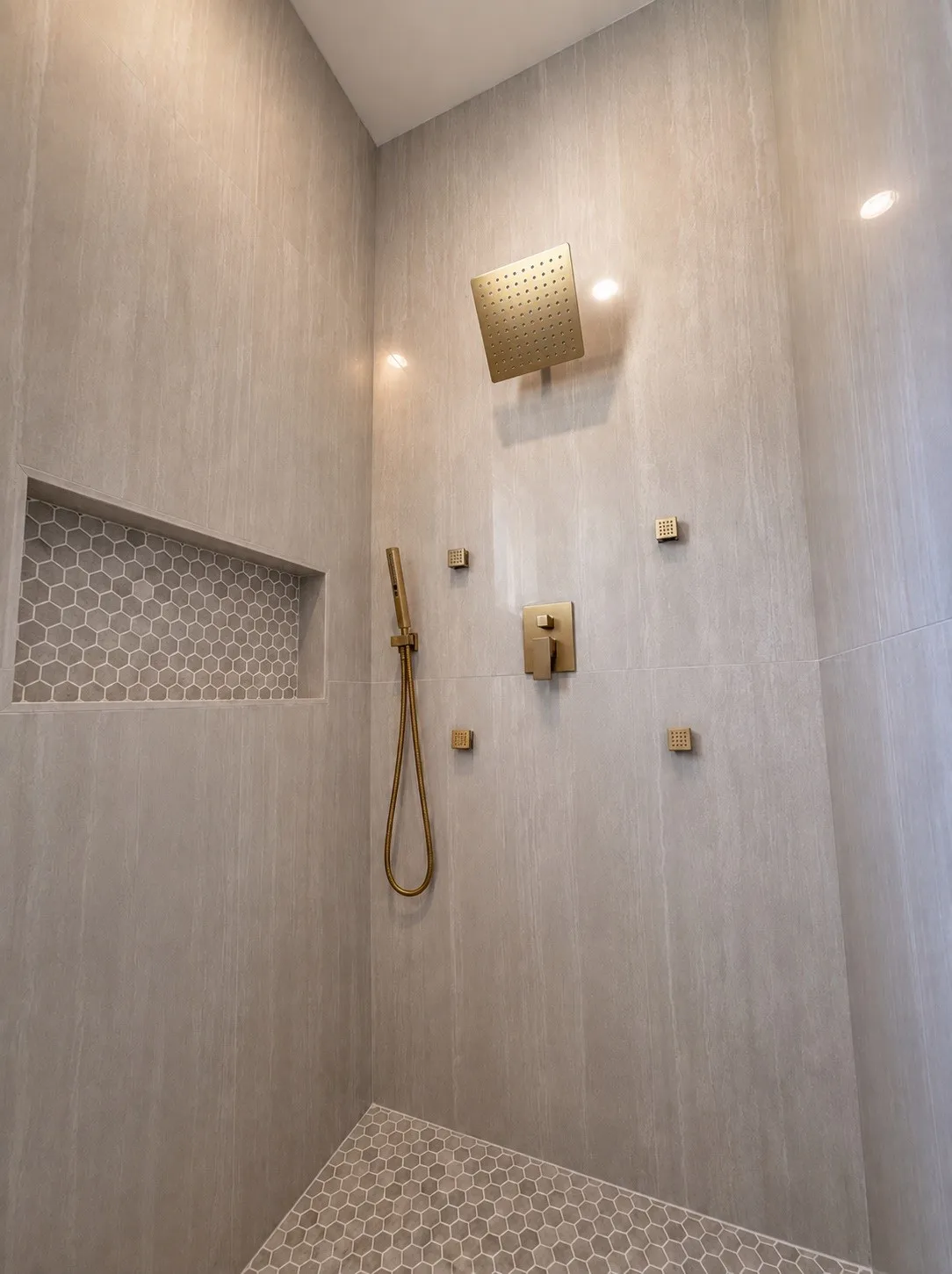 Tiled shower with a rain shower head, hand-held shower, and built-in niche with hexagonal tile