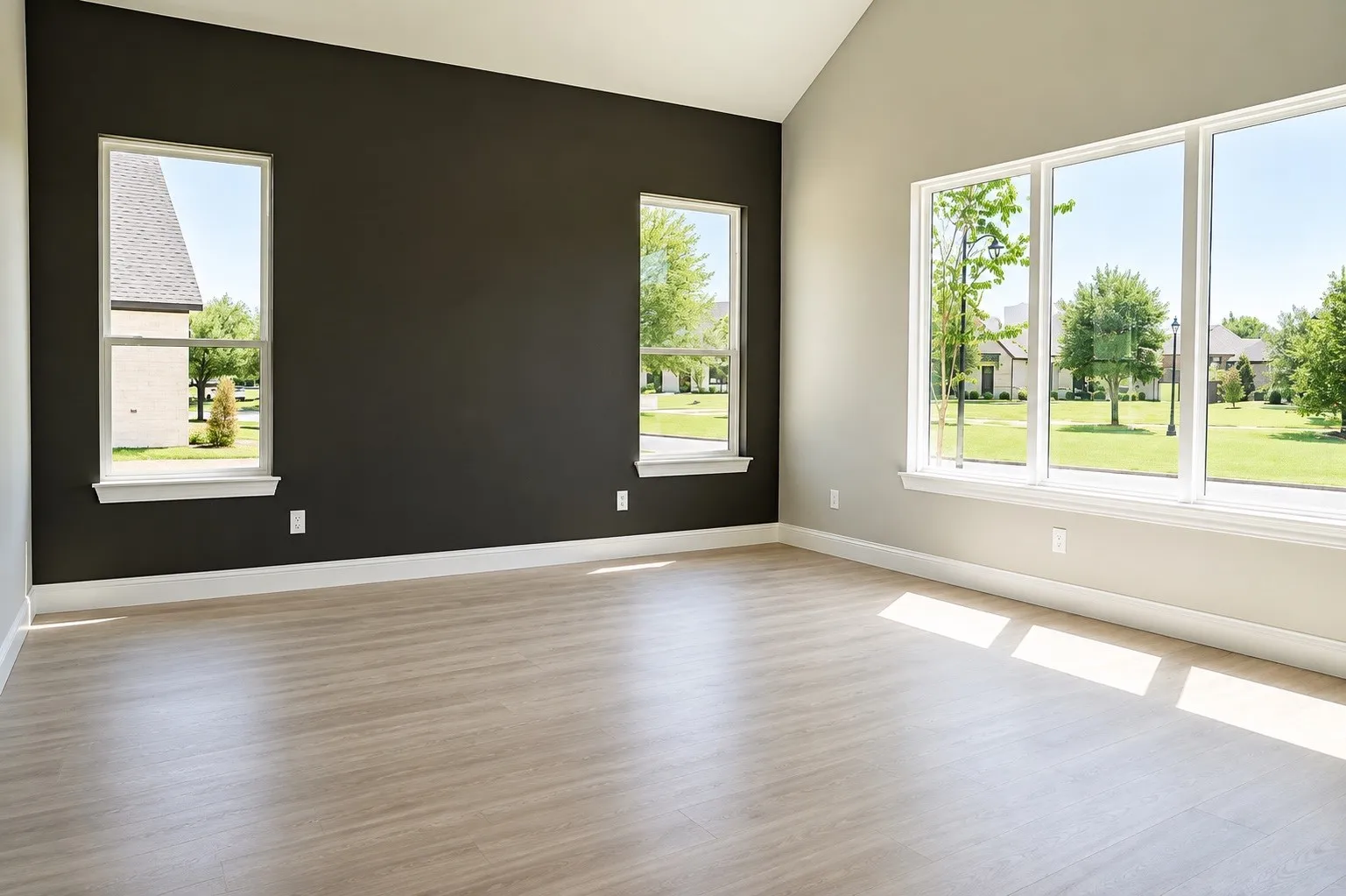 Vaulted ceiling, expansive windows, wood-finish flooring, white trim, and a dark accent wall