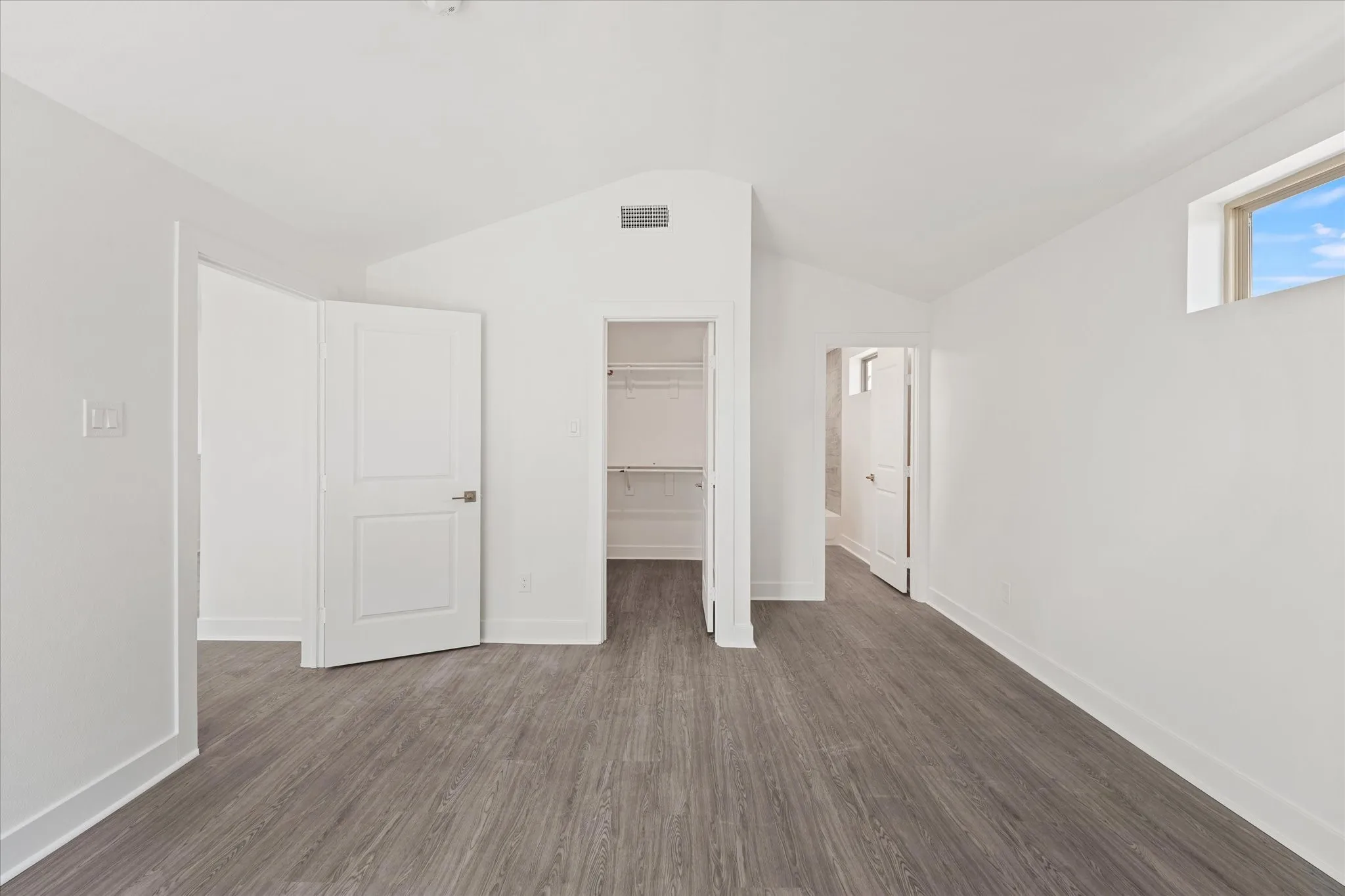 Vaulted ceiling with a high window, wood-finish flooring, white walls, and a built-in closet with shelving